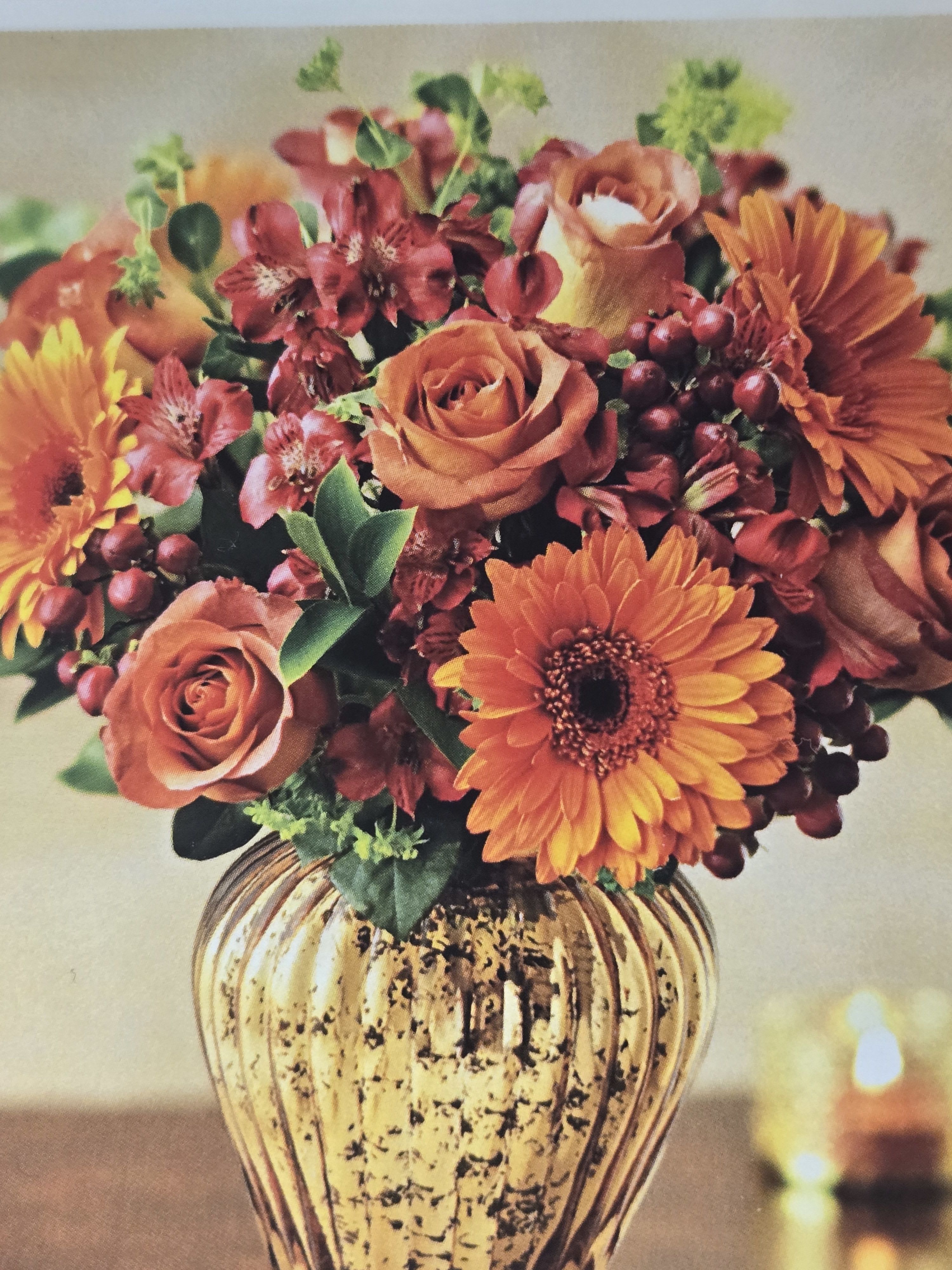 Orange roses and gerbera daisies in a gold vase
