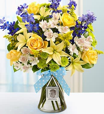 Sweet Baby Boy Arrangement - Product ID: 91363   Celebrate the birth of their sweet baby boy with a beautiful, hand-designed arrangement of roses, lilies, delphinium, alstroemeria and more. Arriving in a stylish glass gathering vase, it comes complete with a magnetic mini photo frame the new parents can use to display a picture of their new arrival. Stunning gathering of fresh roses, lilies, delphinium, alstroemeria, poms, solidago and salal Artistically hand-designed by our select florists in a clear glass gathering vase accented with stylish ribbon; vase measures 8"H Includes a keepsake magnetic mini photo frame Large arrangement measures approximately 22.5"H x 12.5"L Medium arrangement measures approximately 20"H x 11.5"L Small arrangement measures approximately 18.5"H x 10.5"L Our florists hand-design each arrangement, so colors, varieties, and container may vary due to local availability Lilies may arrive in bud form and will open to full beauty over the next 2-3 days