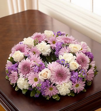 Cremation Wreath - Lavender and White - Product ID: 95423   Lovely in lavender and white, our graceful table wreath arrangement makes a fitting tribute at a cremation service or memorial in the home. Beautifully hand-designed with roses, stock, cremones, carnations and more, it can be elegantly paired with a treasured photograph or cremation urn. Comforting table wreath arrangement of lavender and white blooms such as roses, stock, cremones, carnations, daisy poms and monte casino, gathered with variegated pittosporum and seeded eucalyptus Hand-crafted by our select florists to be sent to the cremation service to honor friends or family members Also appropriate for smaller memorial services in the home The cremation urn or a framed photograph can be placed in the center to present a lovely tribute at the service or home Large arrangement measures approximately 22"H x 22"L Small arrangement measures approximately 17"H x 17"L Our florists hand-design each arrangement, so colors and varieties may vary due to local availability