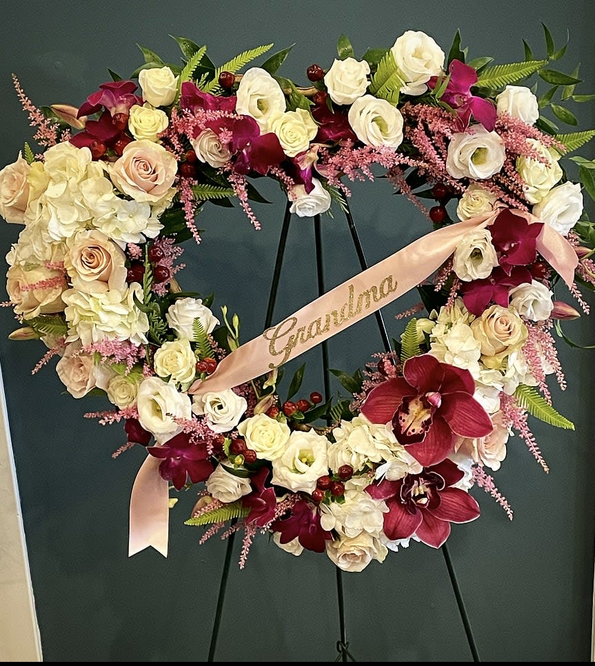 Heart-shaped floral wreath with roses, orchids, and a pink ribbon
