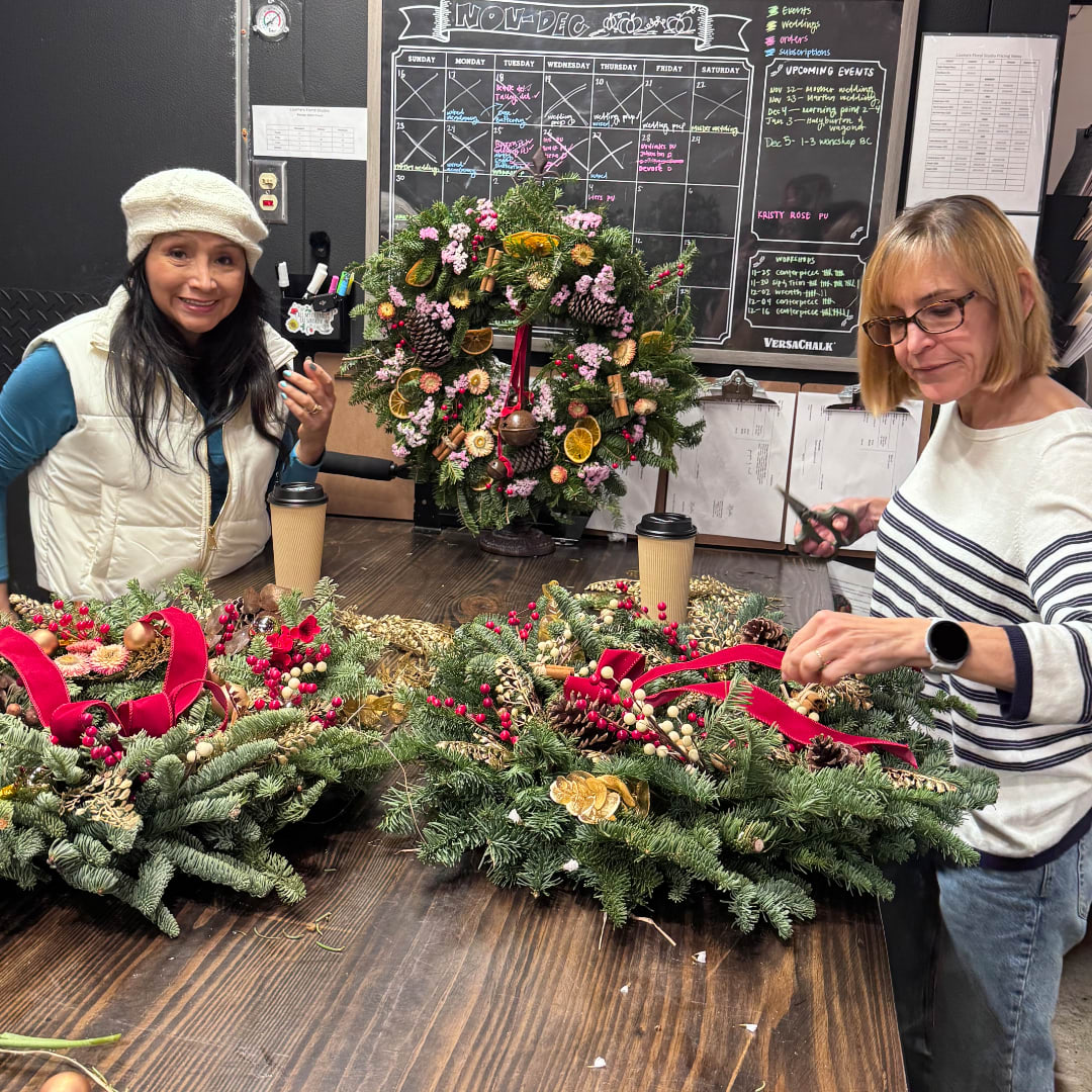 People arranging holiday wreaths with pine, berries, and ribbon on a table