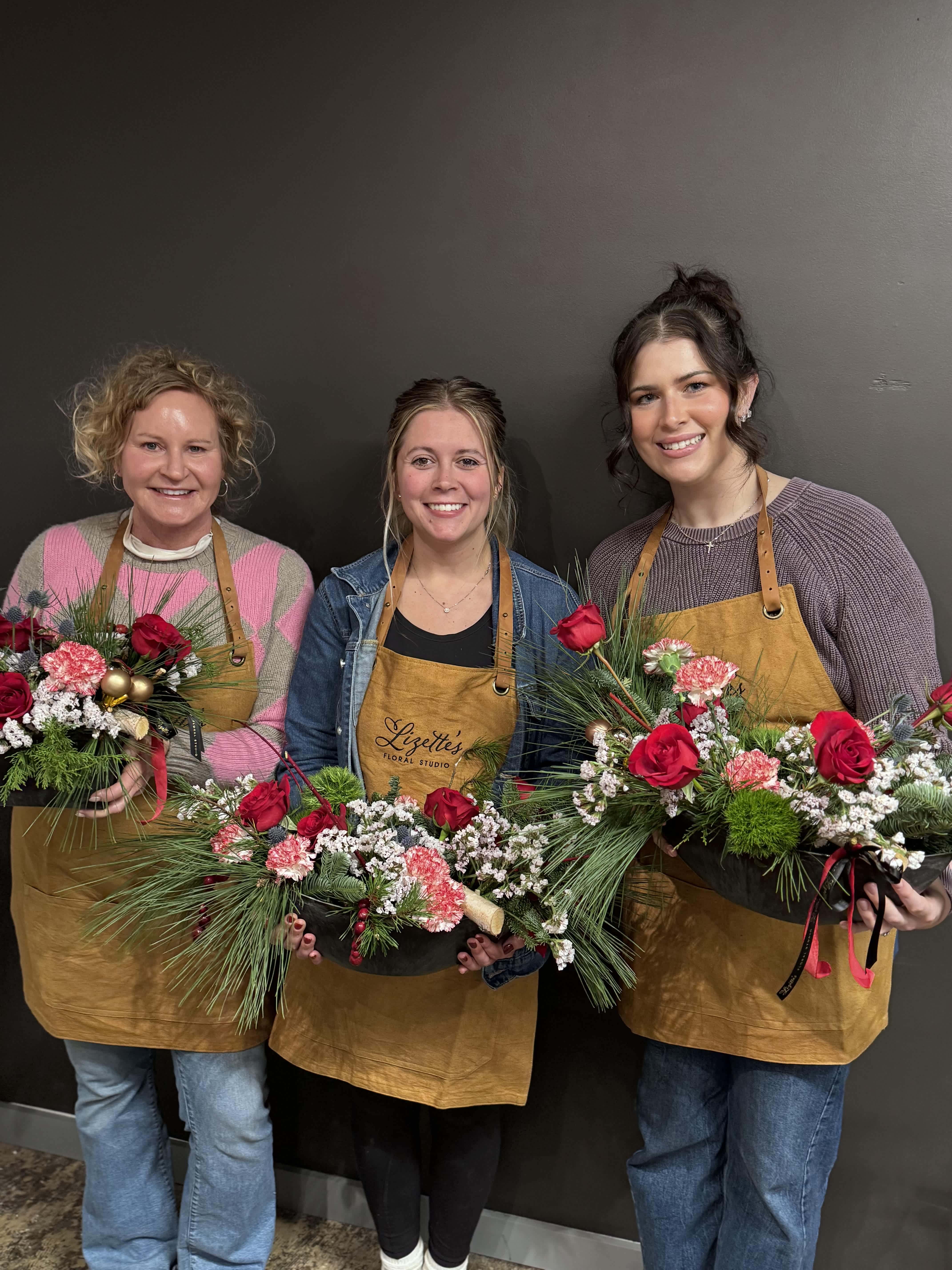 Three women holding holiday floral arrangements in shallow black containers
