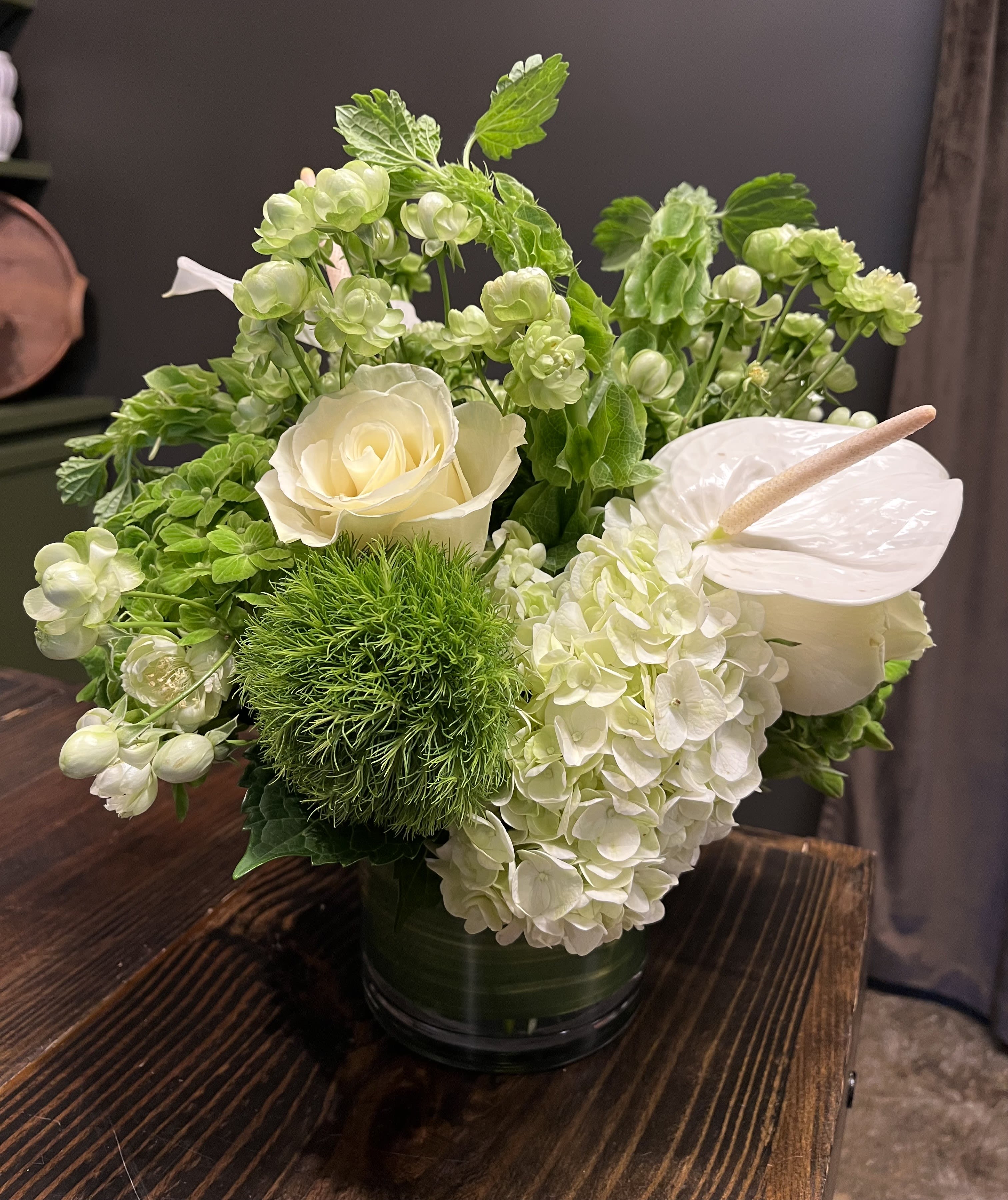 White roses and hydrangeas in a green vase with anthurium and green blooms