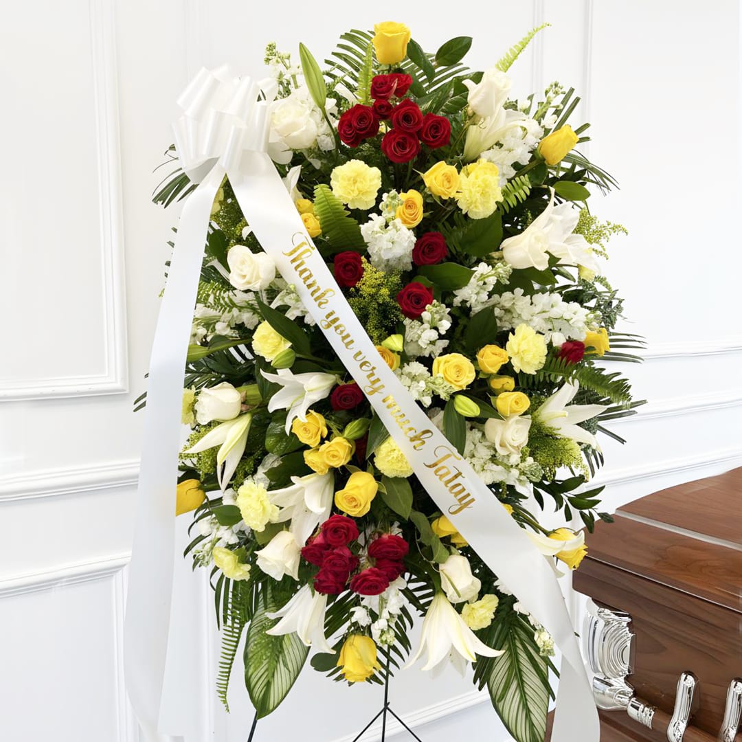 Standing floral spray with red, yellow, and white flowers and a white ribbon