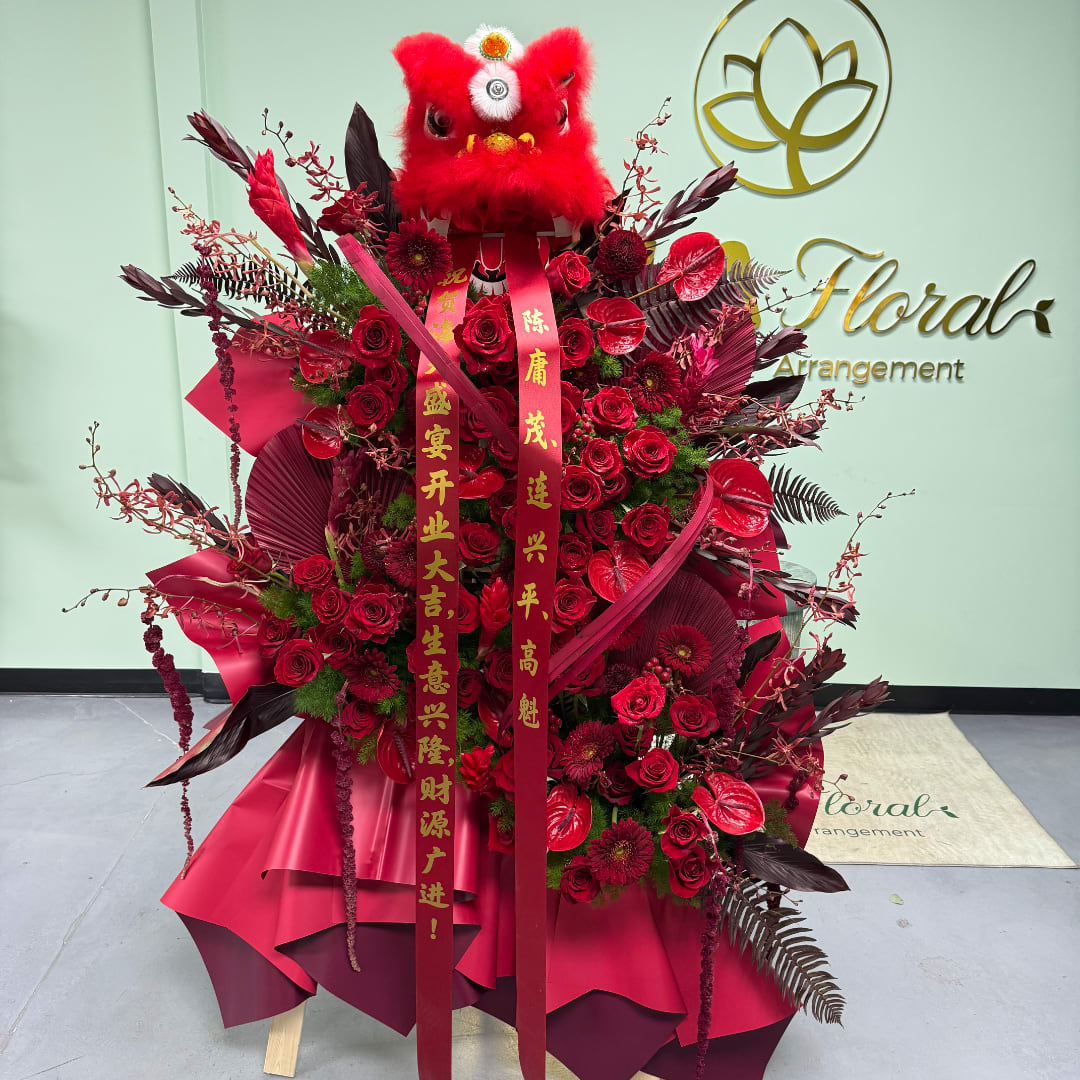 Large red floral arrangement with roses and ribbons, topped by a red lion head decoration