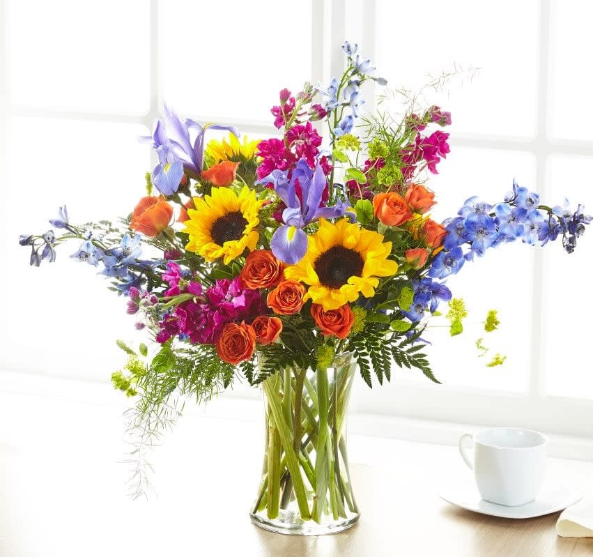 Mixed bouquet of sunflowers, roses, and blue flowers in a glass vase