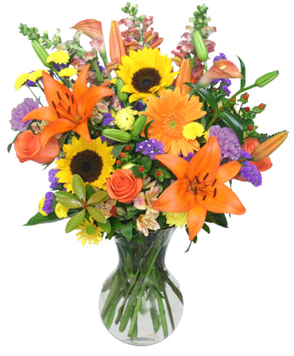 Bright mixed bouquet with sunflowers, orange lilies, and roses in a glass vase