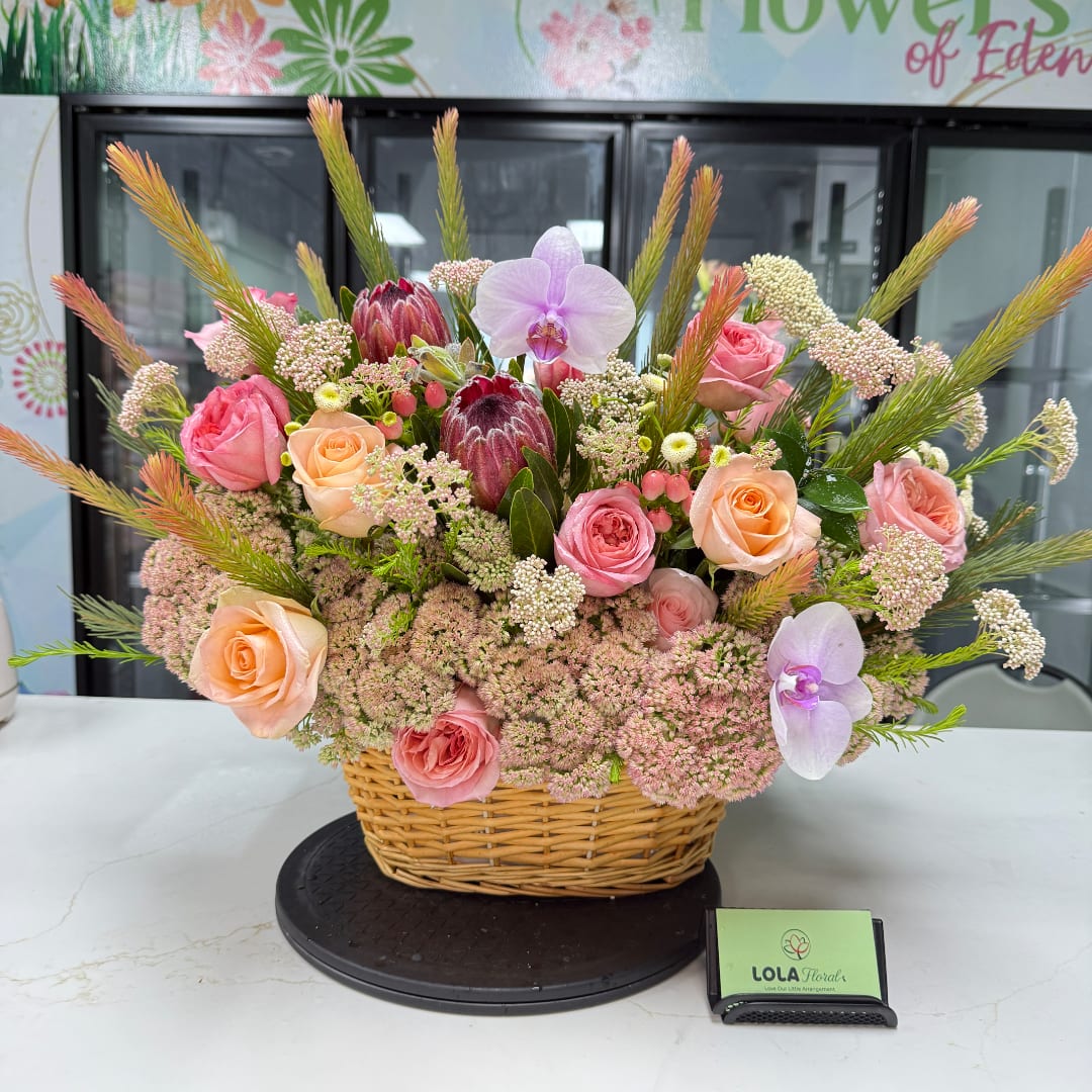 Basket arrangement of pink and peach roses with orchids and protea