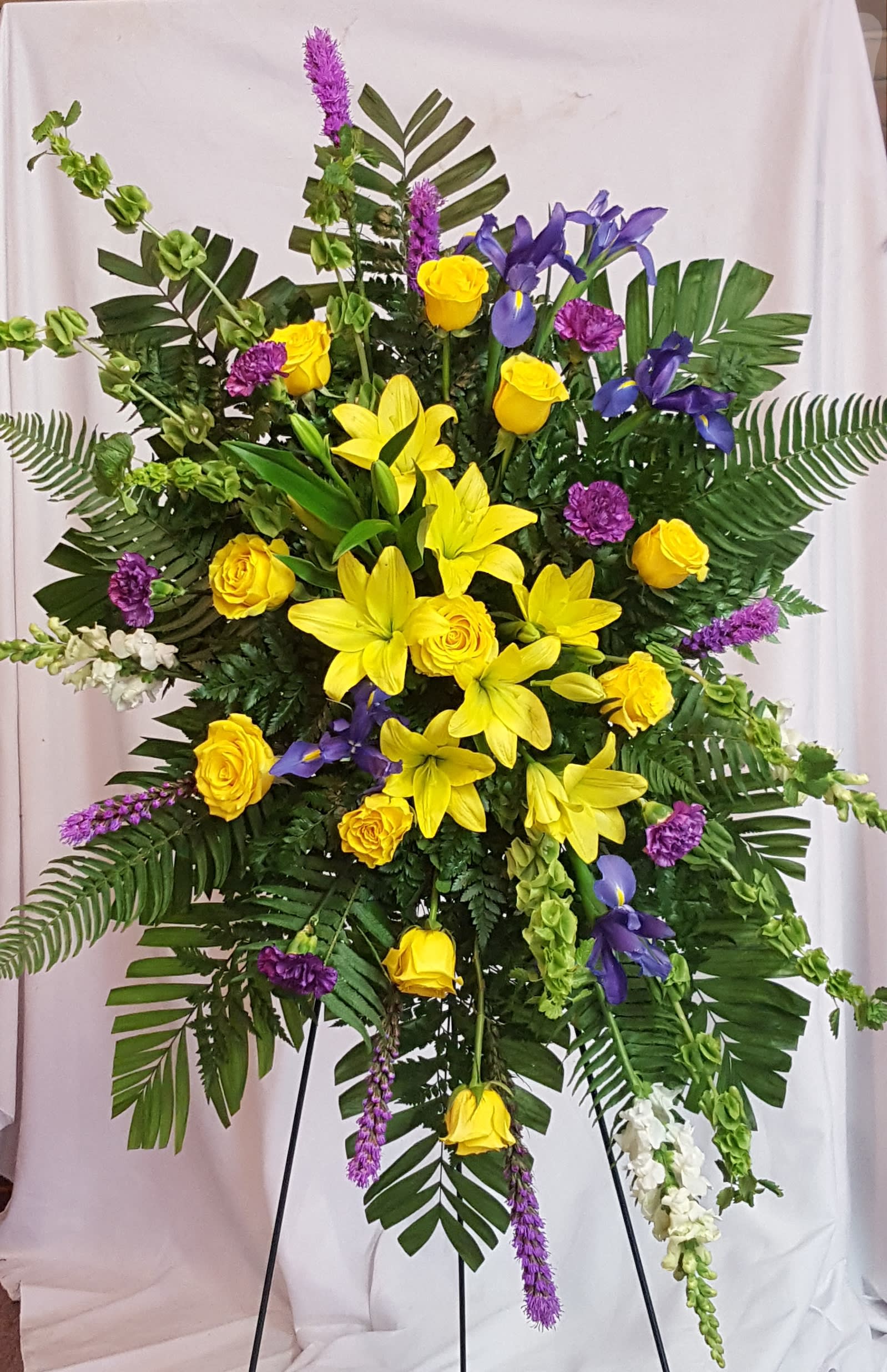Large standing floral spray with yellow roses, lilies, and purple flowers