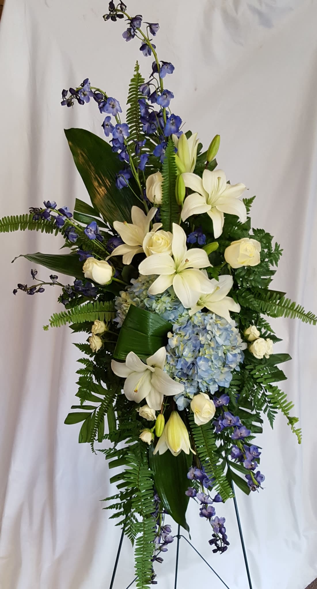 Tall floral standing spray with white lilies, roses, blue hydrangea, and purple delphinium