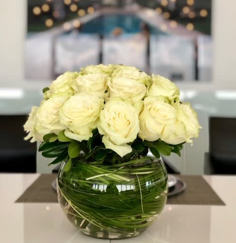 White roses arranged in a round glass vase with green stems visible inside