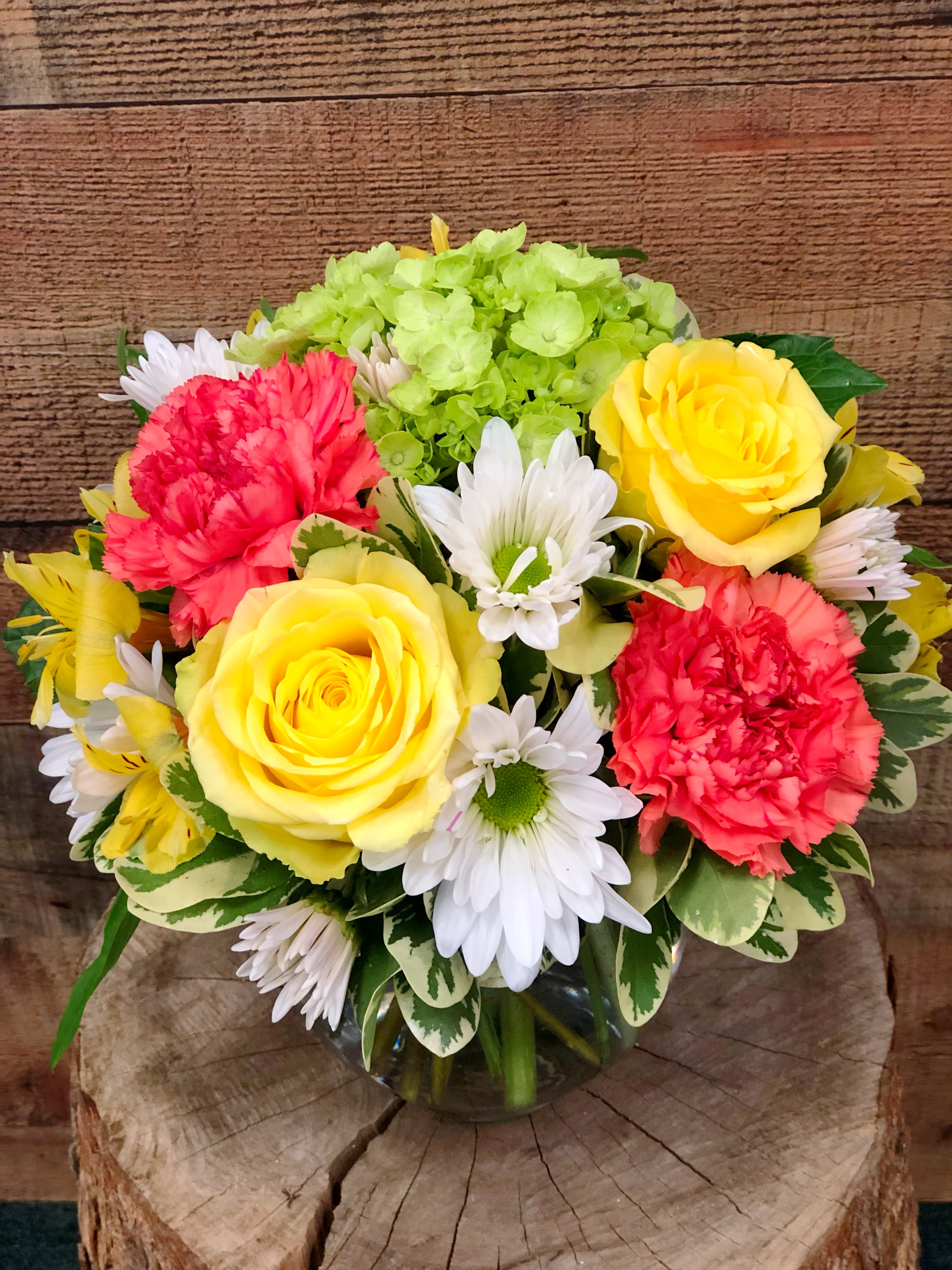 Bouquet of yellow roses, red carnations, white daisies, and green hydrangea in a glass vase