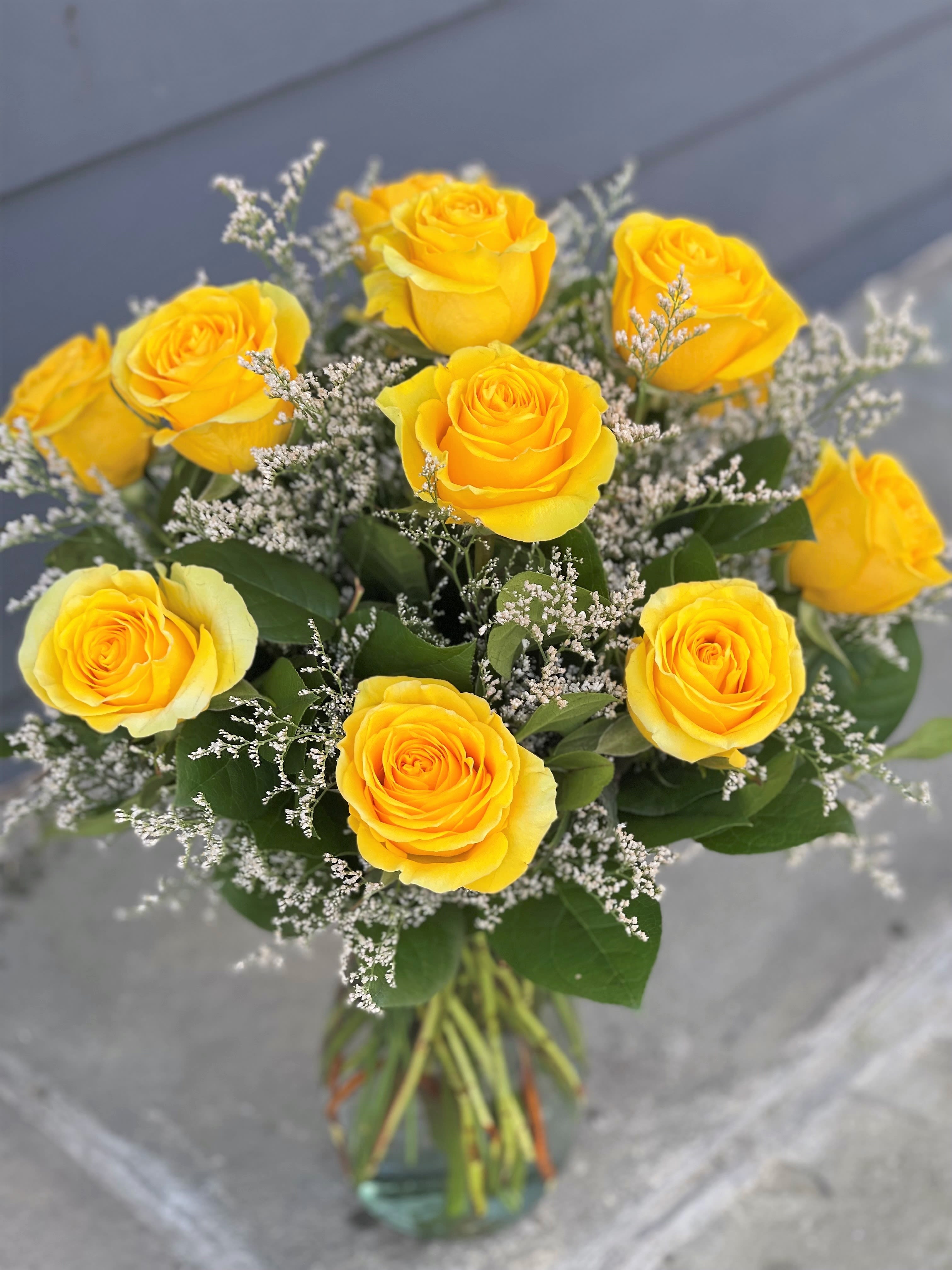 Premium Dozen Yellow Roses - 12 Premium long stem yellow roses artfully arranged in a recycled clear glass vase with greens and seasonal filler.