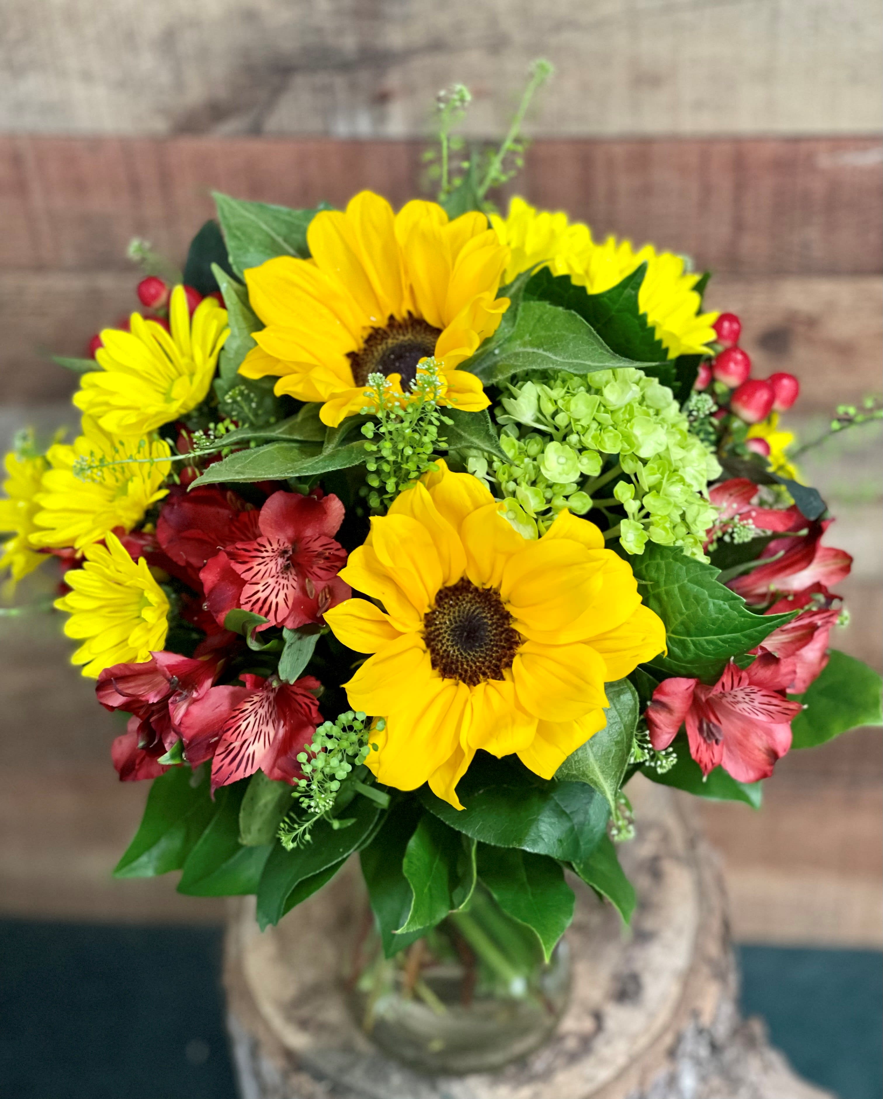 Sunny Garden Bouquet - Smiling sunflowers are arranged with bold summer colors in a simple clear vase. Paired with hydrangea and long lasting alstroemerias, this will bring sunshine to any summer gathering.