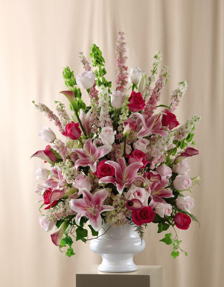 FTD Solemnity Arrangement - The FTD® Solemnity Arrangement is the perfect accent piece for the  ceremony or reception. Hot pink roses pop against a backdrop of pink  roses, larkspur, mini calla lilies, delphinium, hydrangea, and Oriental  Lilies accented with Bells of Ireland and an assortment of fresh, lush  greens. Perfectly arranged in a white plastic urn, this presentation  will fill the space your exchange your vows or celebrate with the colors  and sweetness of true love. Approx. 40âH x 29âW. 