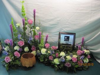 Floral arrangement with pink roses and tall purple spikes around a framed plaque