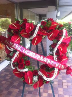 Large red floral standing wreath on an easel with a pink ribbon