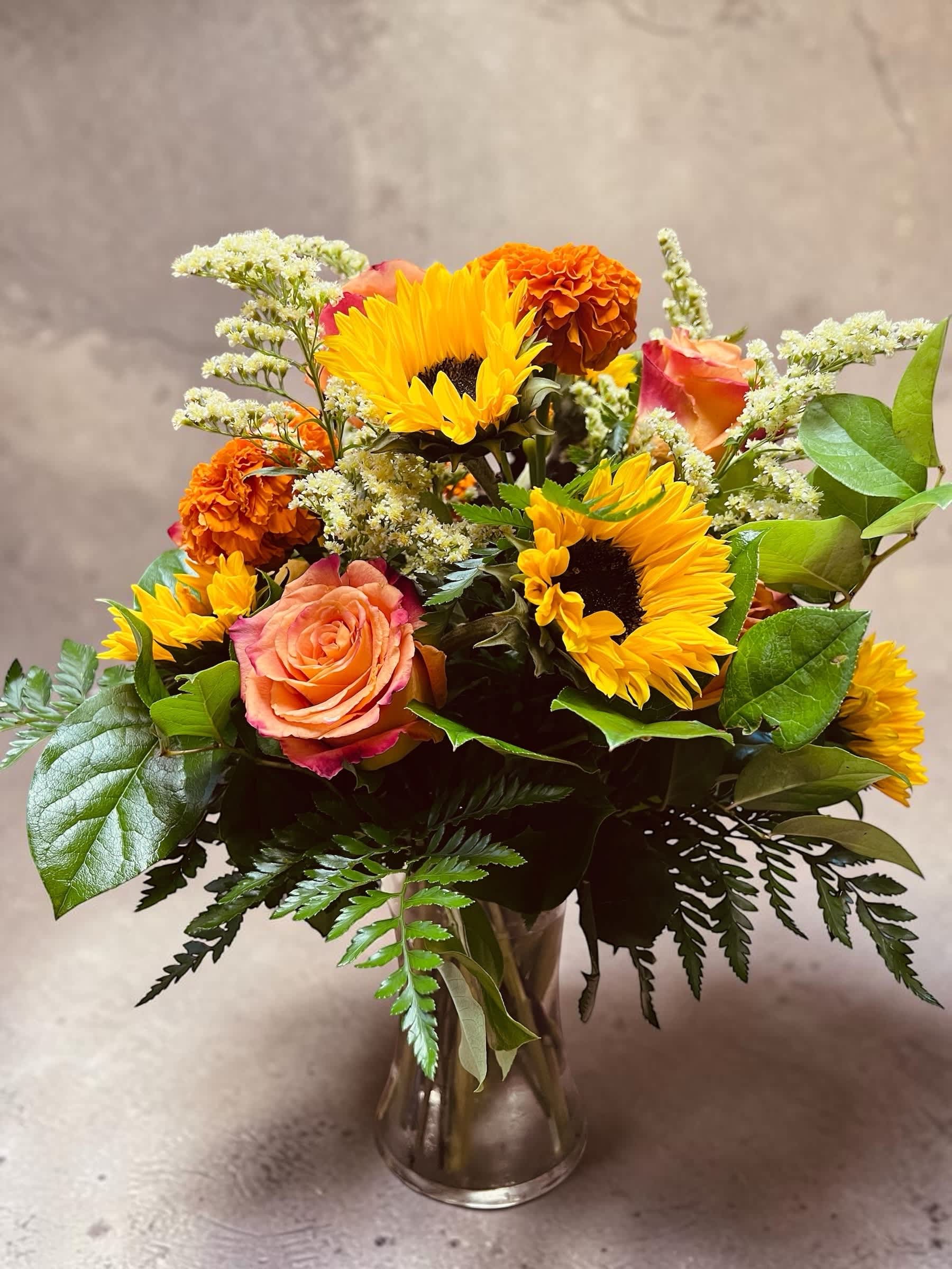 Bouquet of sunflowers, roses, and orange carnations in a glass vase