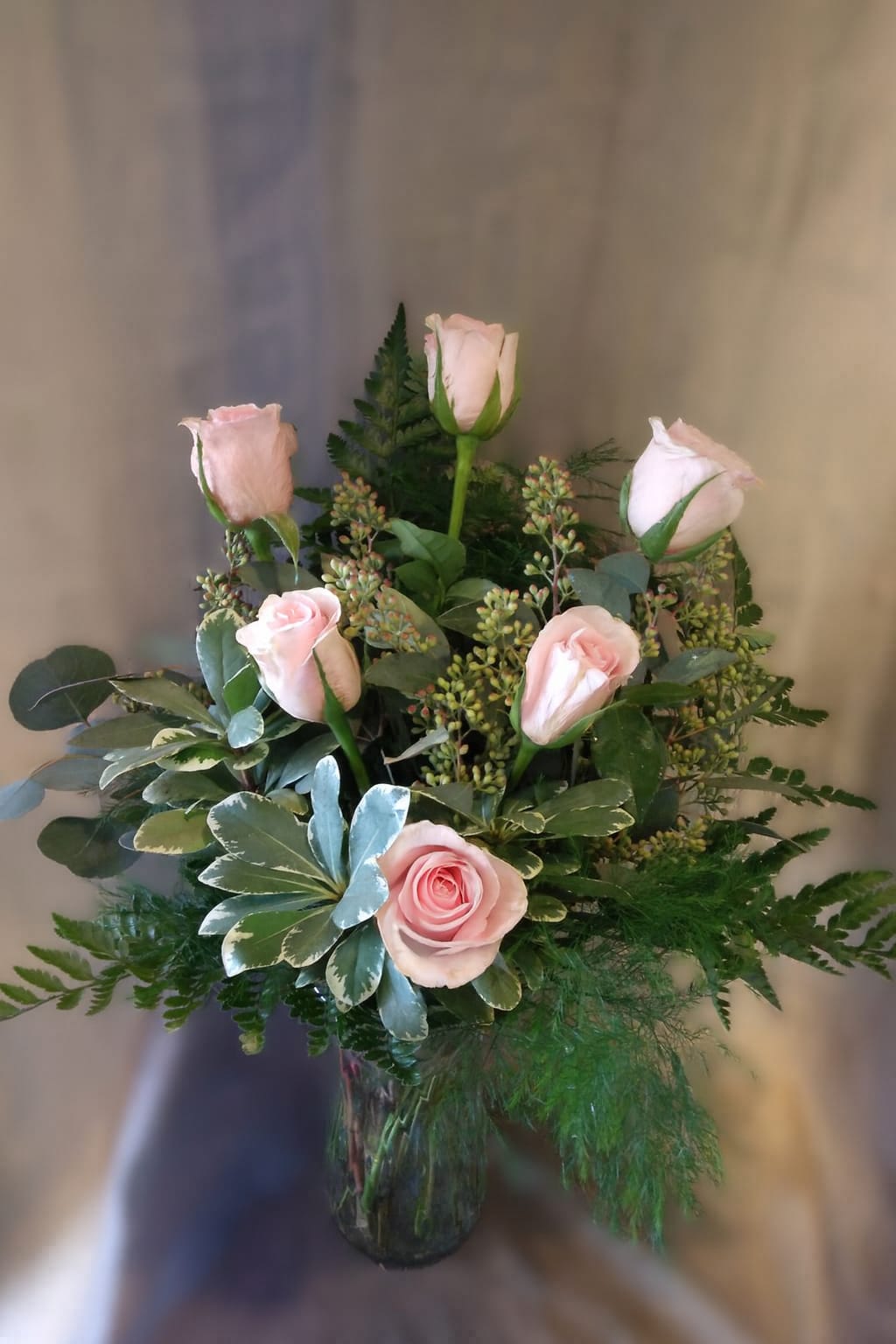 Pink roses arranged in a glass vase with mixed greenery.