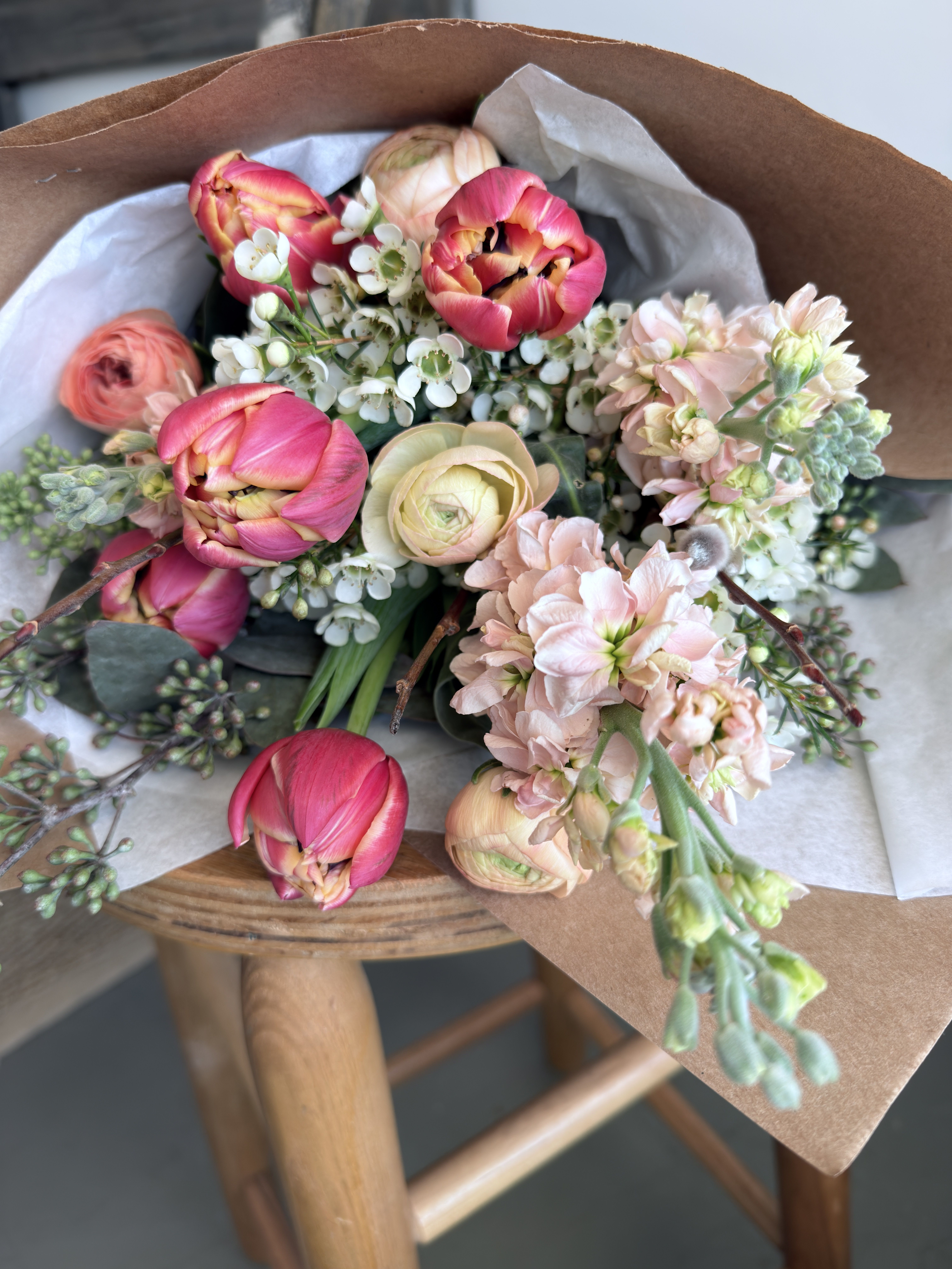 Bouquet of pink tulips and pale flowers wrapped in brown paper