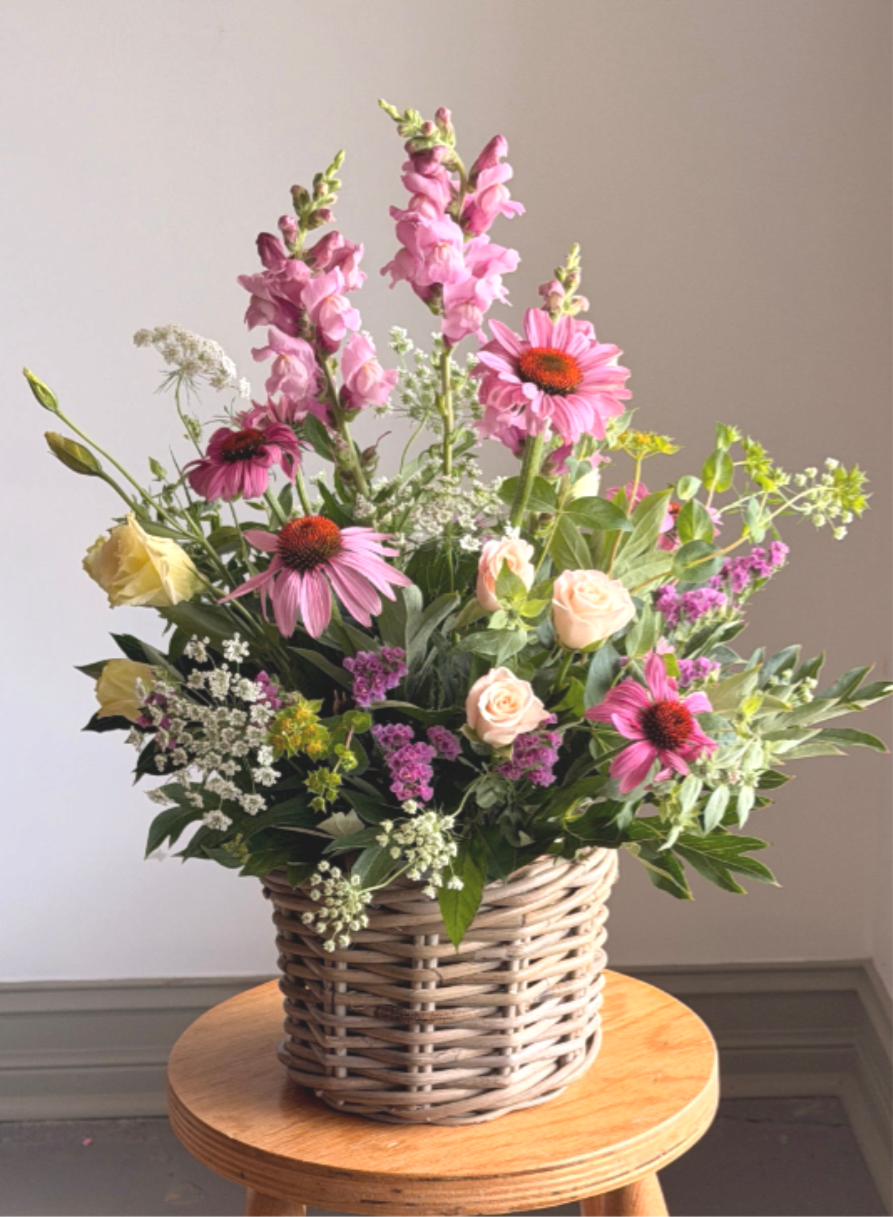 Garden Party - Share summer's bounty with this garden party bouquet. Tall snapdragons ride above a lively mix of garden roses, echinacea and lisianthus. Arranged in a woven wicker basket, this garden style bouquet is full and airy with varied heights and fragrant foliage for a slightly wild, natural texture. It's the perfect addition to any summer celebration. 