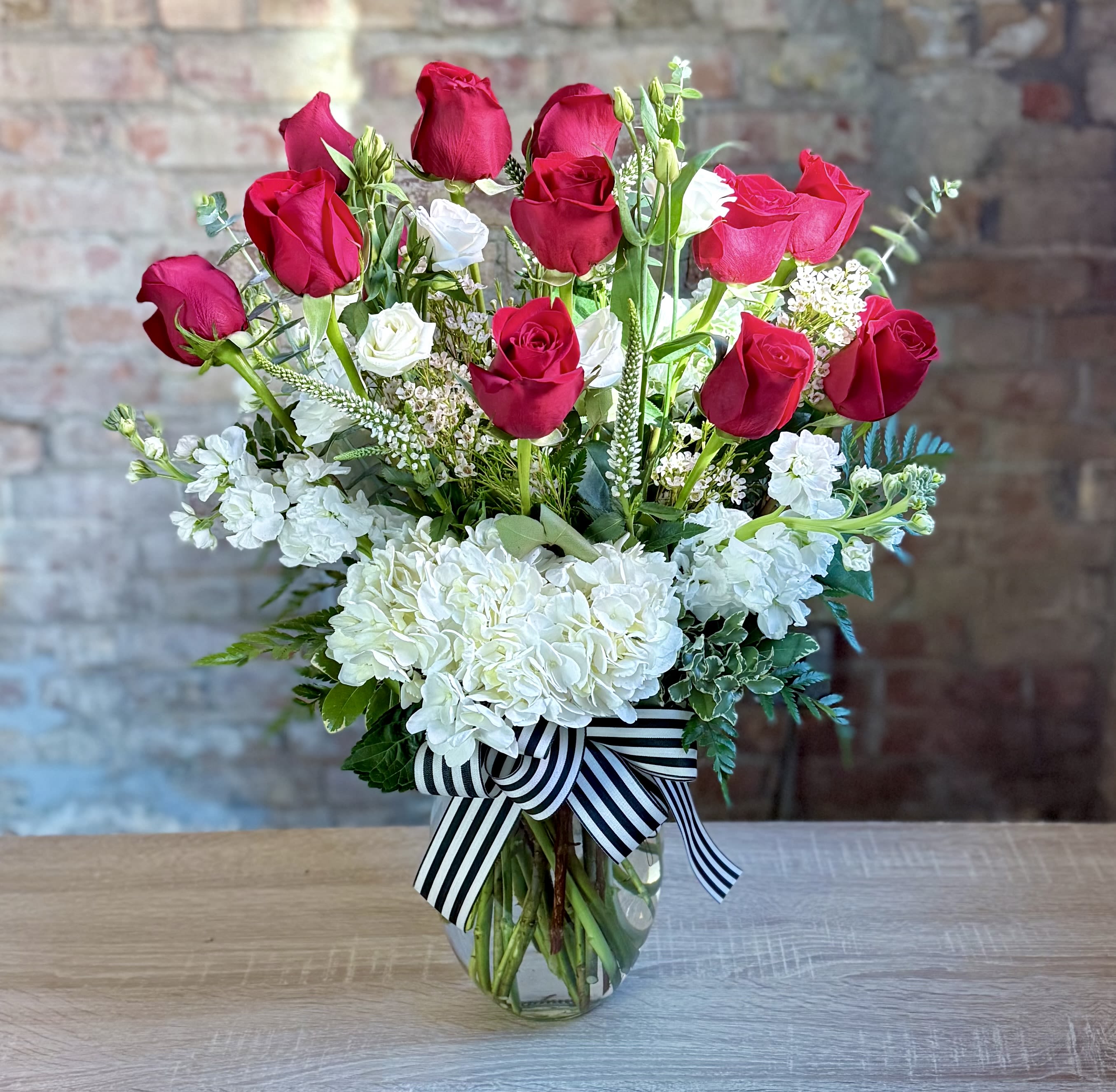 Red and white roses arranged in a glass vase with a striped ribbon