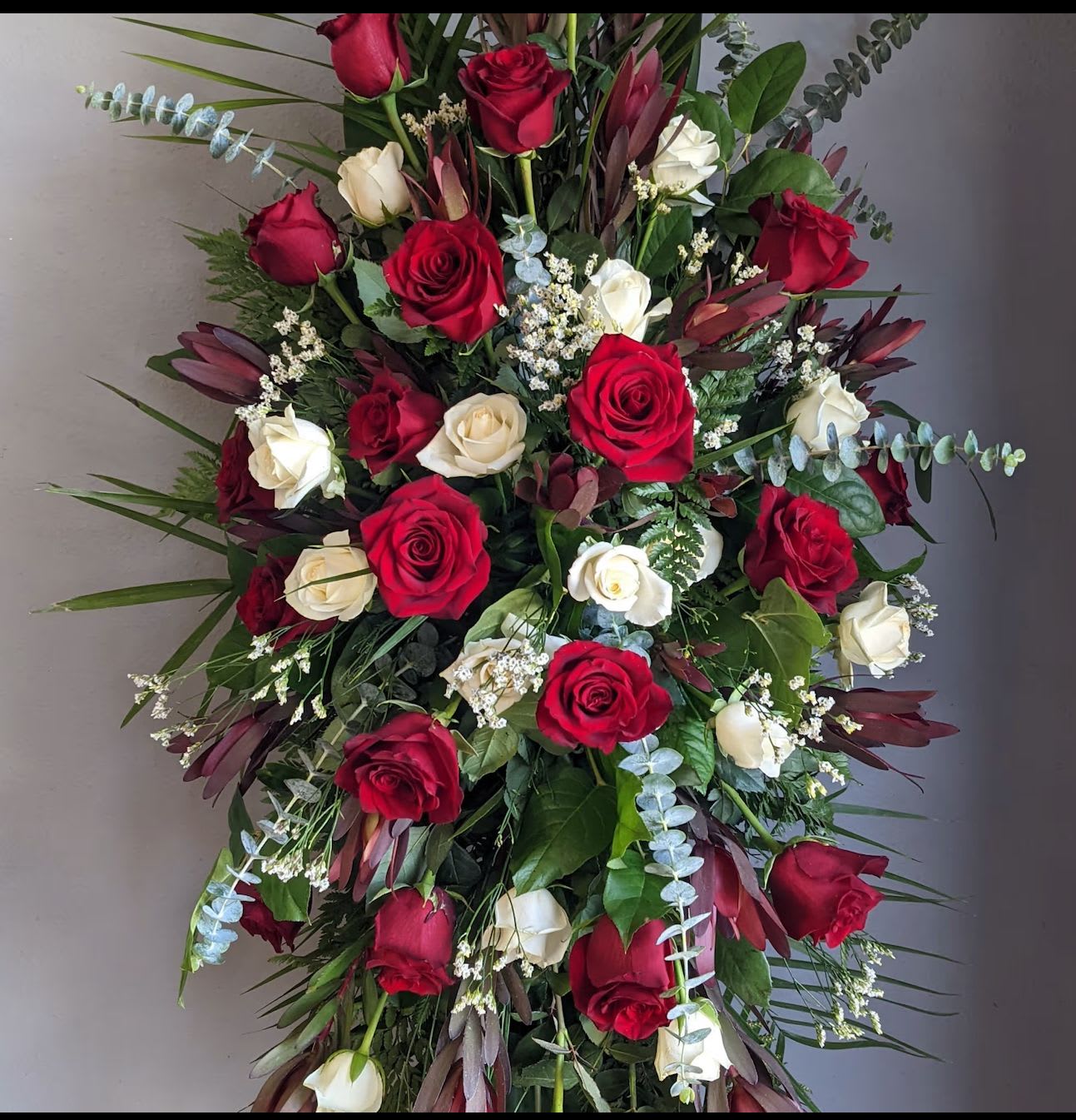 Deeply Admired Standing Spray - Featuring a thoughtful blend of red and white flowers, this arrangement conveys love, respect, and remembrance. Accented with soft greenery and presented on an easel, Deeply Honored offers comfort and a heartfelt expression of sympathy during services or memorial gatherings.