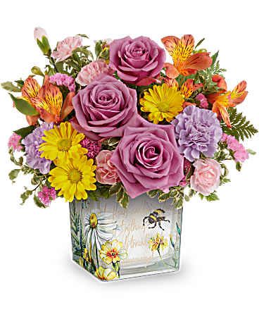 Buzz Bouquet - Like a bee dancing through a hidden garden, this enchanting bouquet of orange, lavender, and yellow blooms in a vintage-inspired glass cube makes for a truly magical gift. This delightful arrangement features vibrant orange alstroemeria, lavender carnations, miniature pink carnations, yellow daisy spray chrysanthemums, and pink sinuata statice, all beautifully accented with leatherleaf fern and pitta negra. It is presented in Teleflora's Floral Buzz Cube, making it a charming addition to any tablescape. Orientation: All-Around 