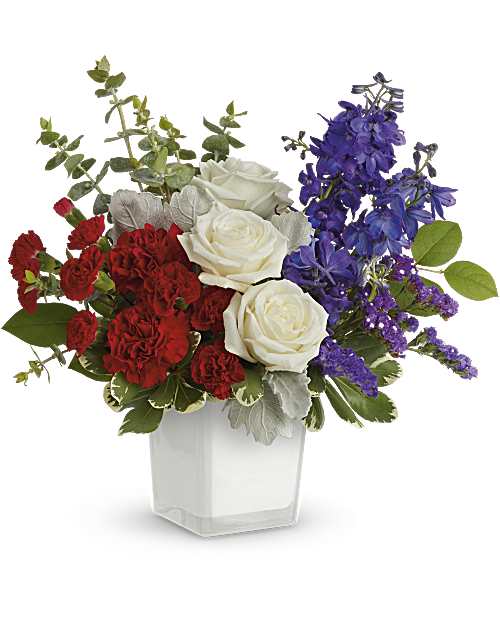 Red carnations, white roses, and purple flowers in a clear square vase