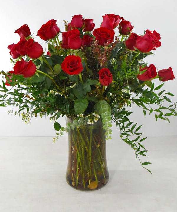 Red roses arranged in a clear glass vase with greenery