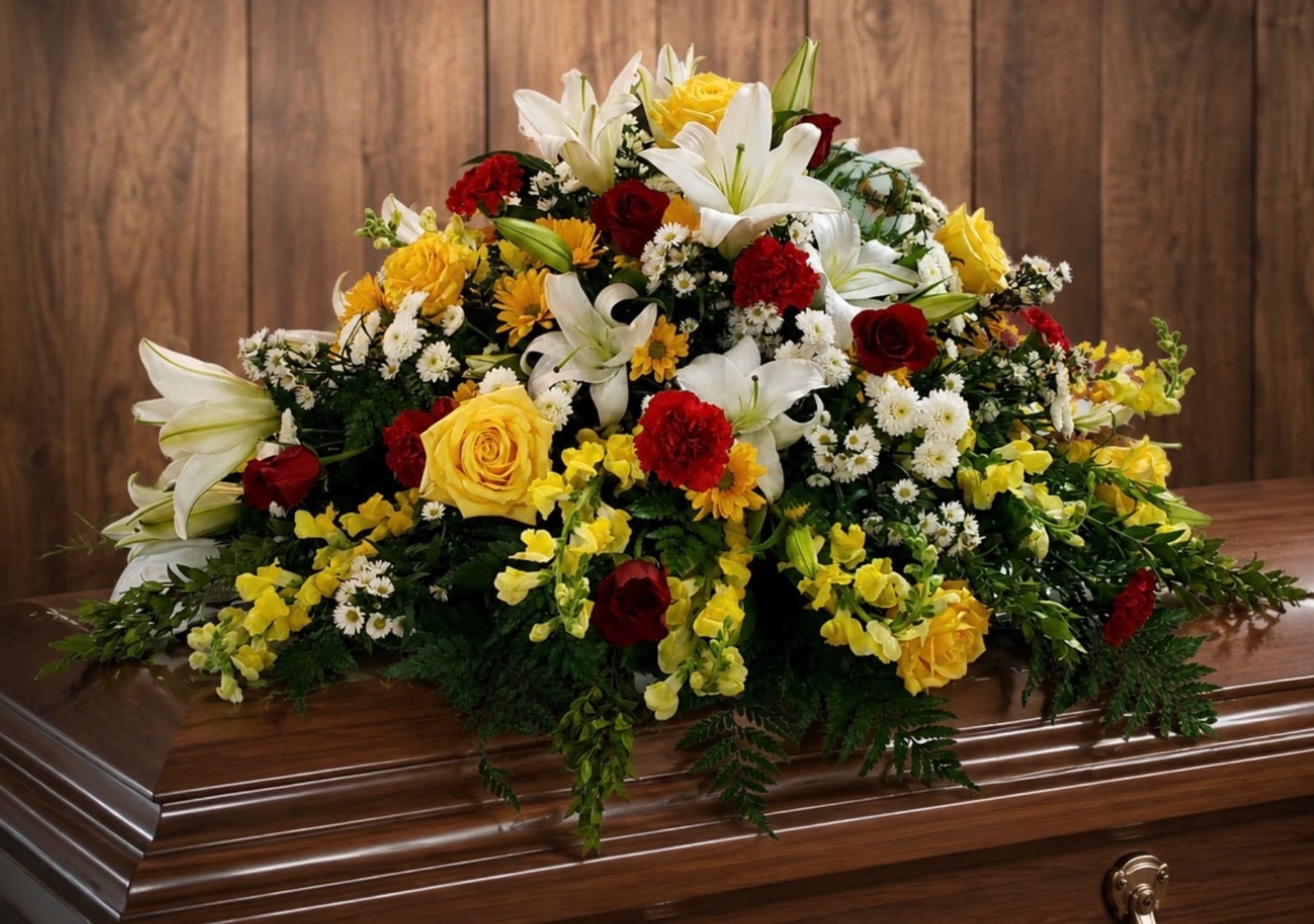 Large floral casket spray with white lilies, yellow roses, and red carnations