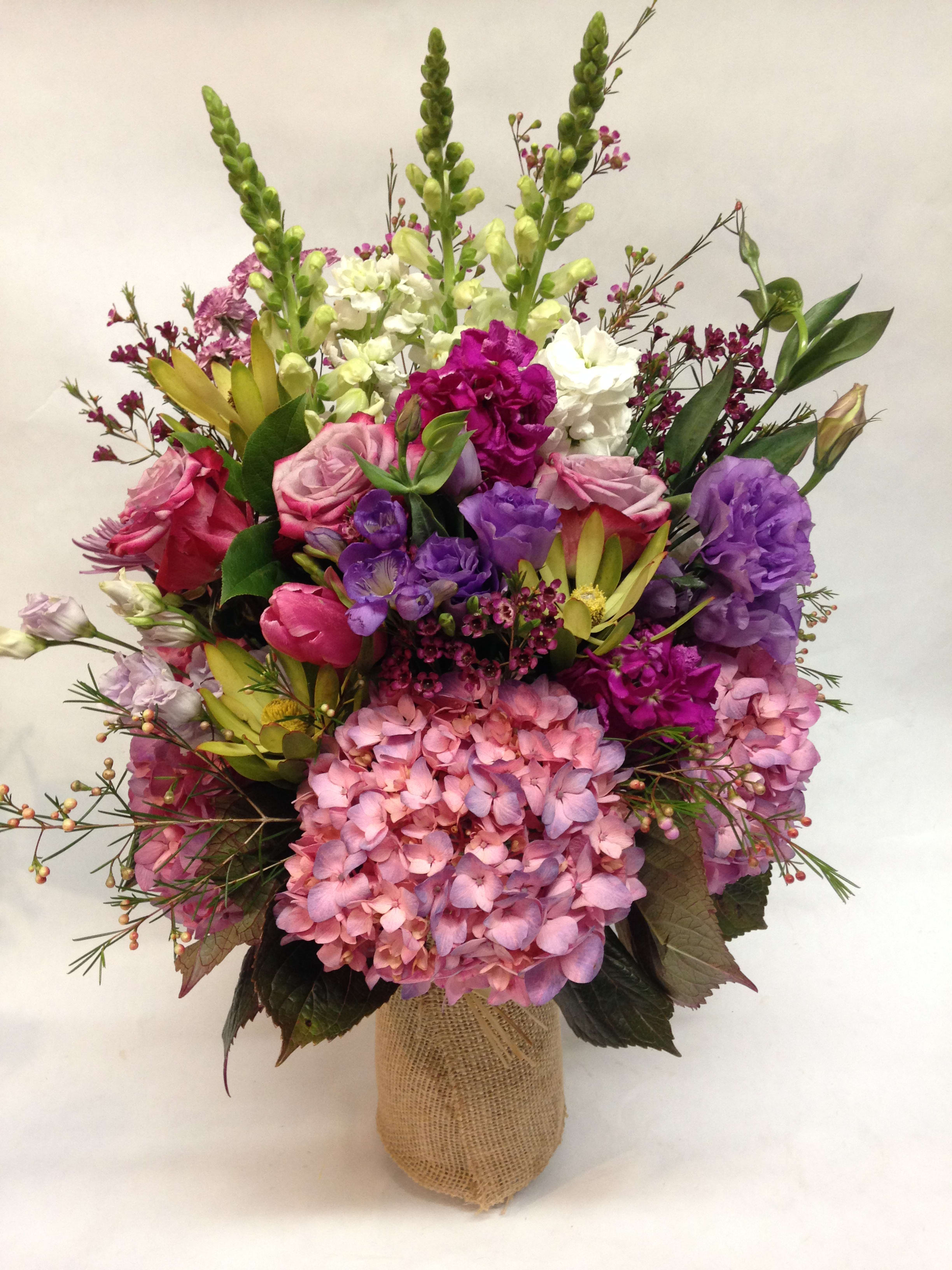 Mixed bouquet of pink, purple, and white flowers in a burlap-wrapped vase