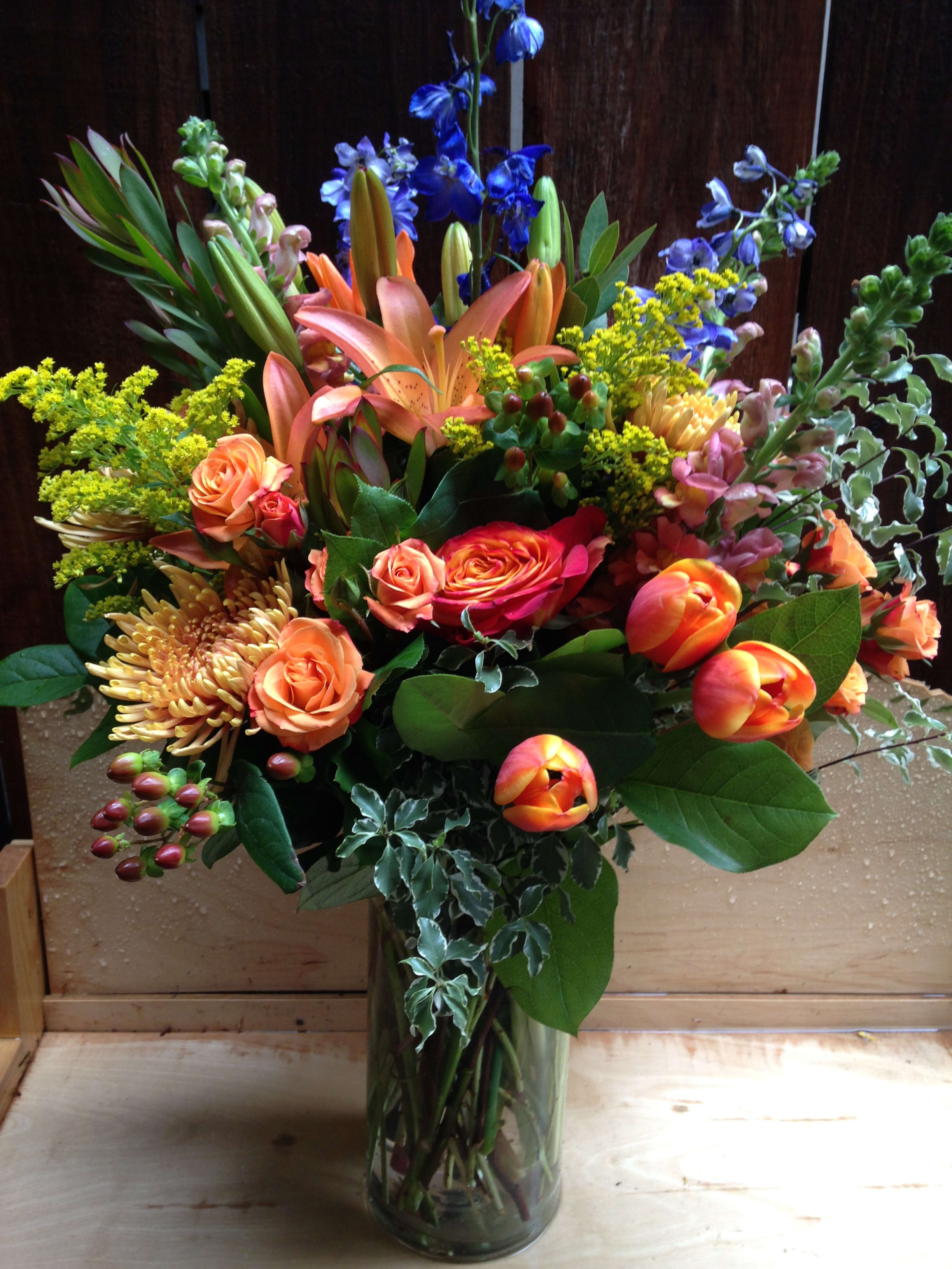 Mixed bouquet of orange, blue, and yellow flowers in a glass vase