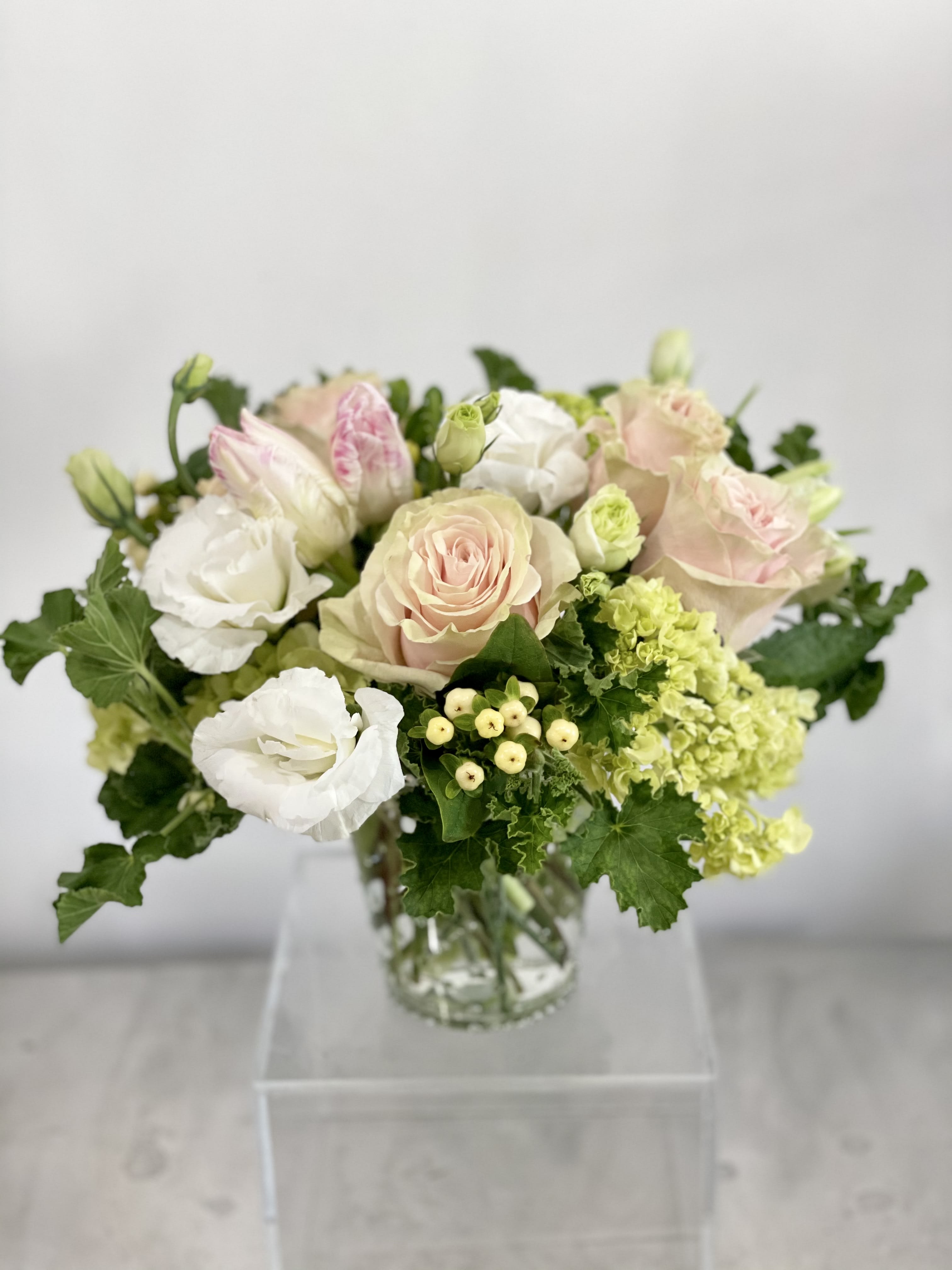 Pastel roses and white blooms arranged in a clear glass vase