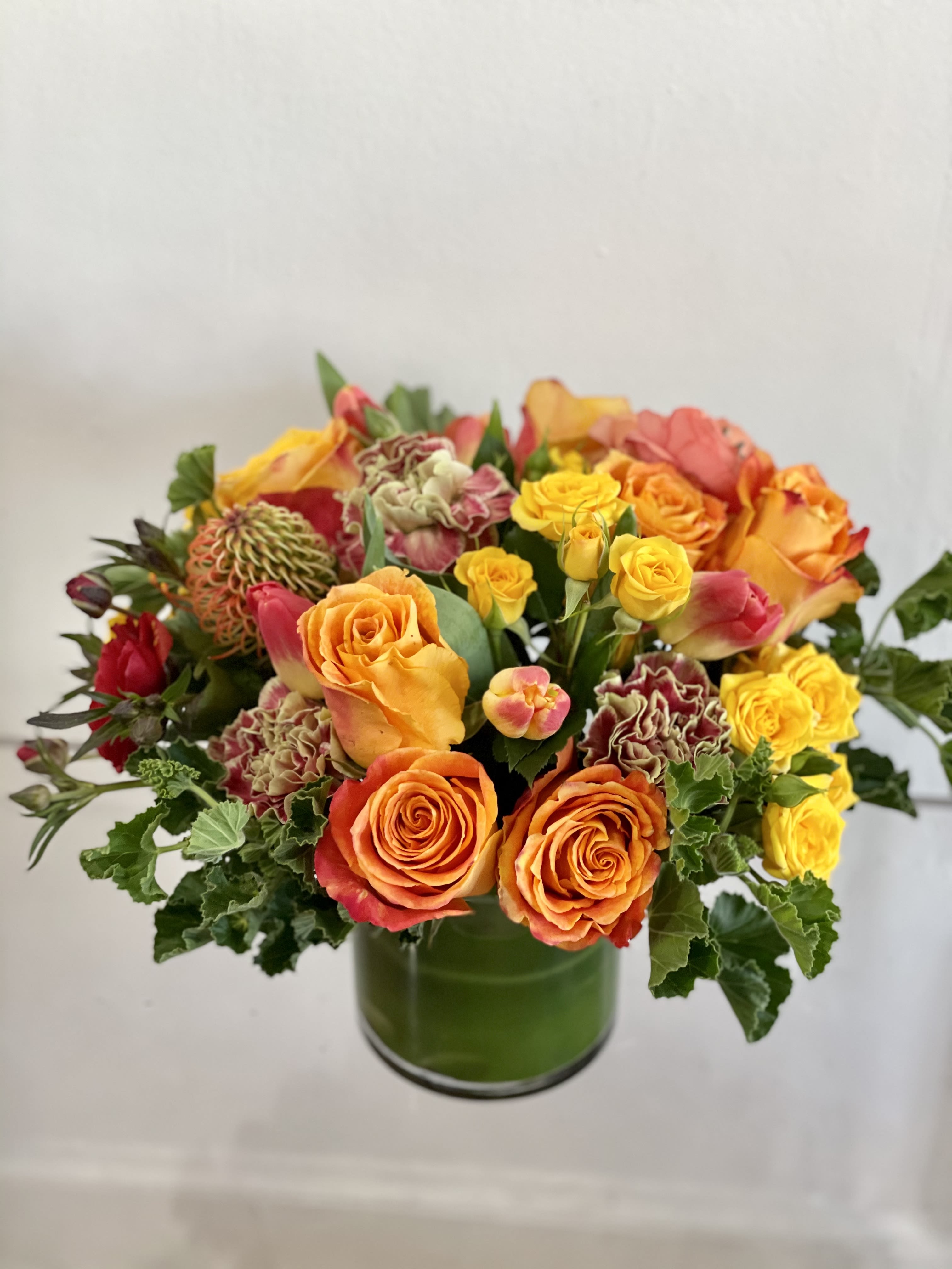 Here comes the Sun - A burst of sunshine! This is a textured luxe mix of the best of spring from local farms in oranges and yellow. This designers choice bright centerpiece is sure to be loved by one happy recipient. We will choose all the blooms in this palette to give your loved one a beautiful bright arrangement.  NOTES: We will choose the freshest and most interesting ingredients at the market to make this arrangement shine. Vessel may be substituted depending on availability.   If any design element such as color or flower/foliage are very important to your order please contact us to ensure availability first by calling the shop at  415 751 2747  Standard- (PICTURED) Side table, desk, vanity, Standard small.  Deluxe- Dinner table, coffee table   Premium- Premium blooms added and it will have the largest footprint suitable for a large coffee table, entry way, or credenza  