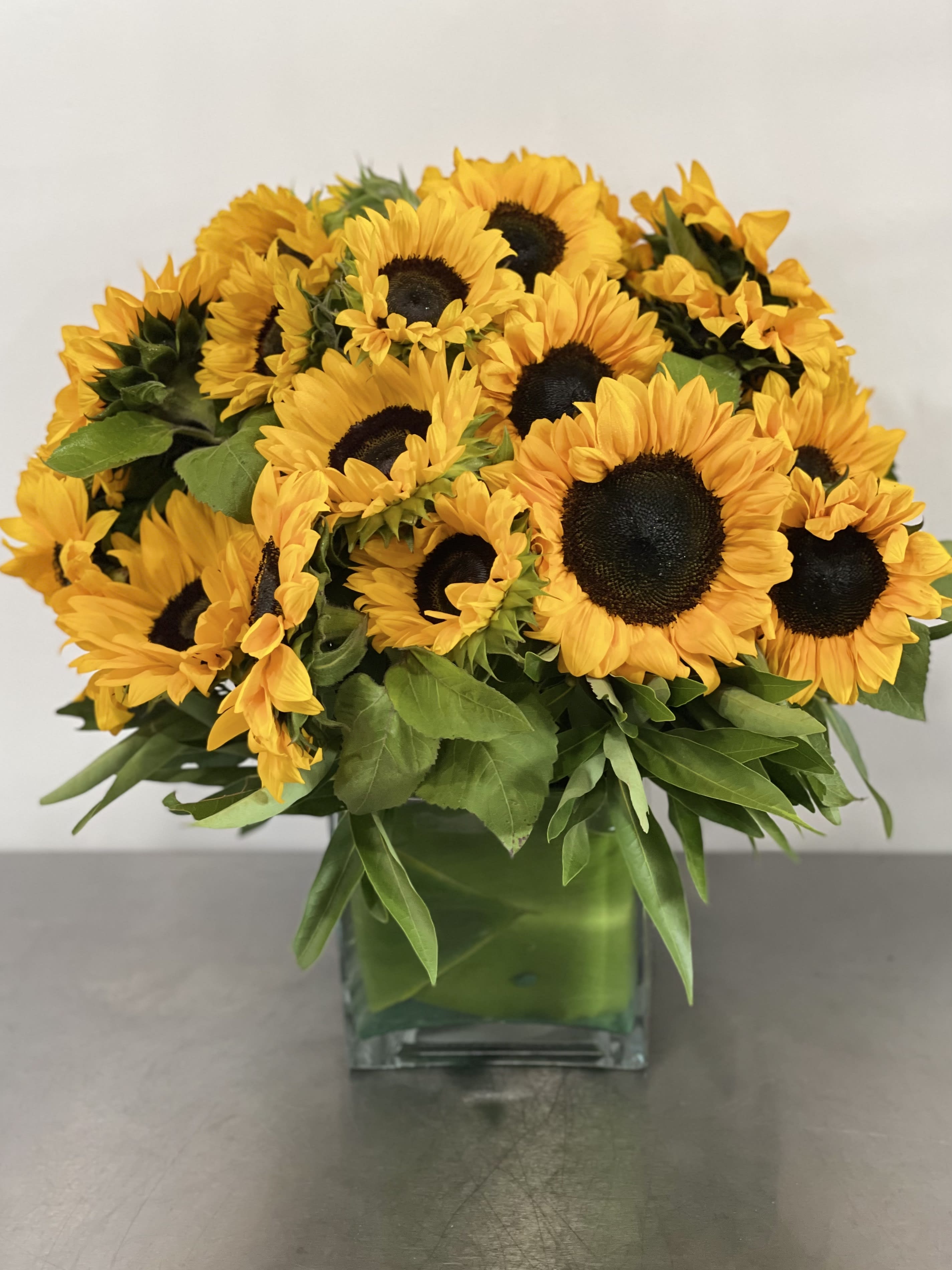 Sunshine in Vase  - Send happy sun flowers the right way! This bouquet makes quite the impression with almost 3 dozen sunflowers in a ti leaf lined vase. This arrangement is for the person who loves sunflowers the modern way.  This style florals can be made in three sizes:  Saturday and Same Day are available if you call the shop.   ** 415 751 2747 10:00AM -5:00PM   