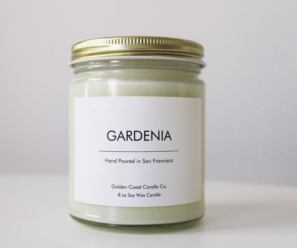 A gardenia-scented candle in a glass jar with a gold lid