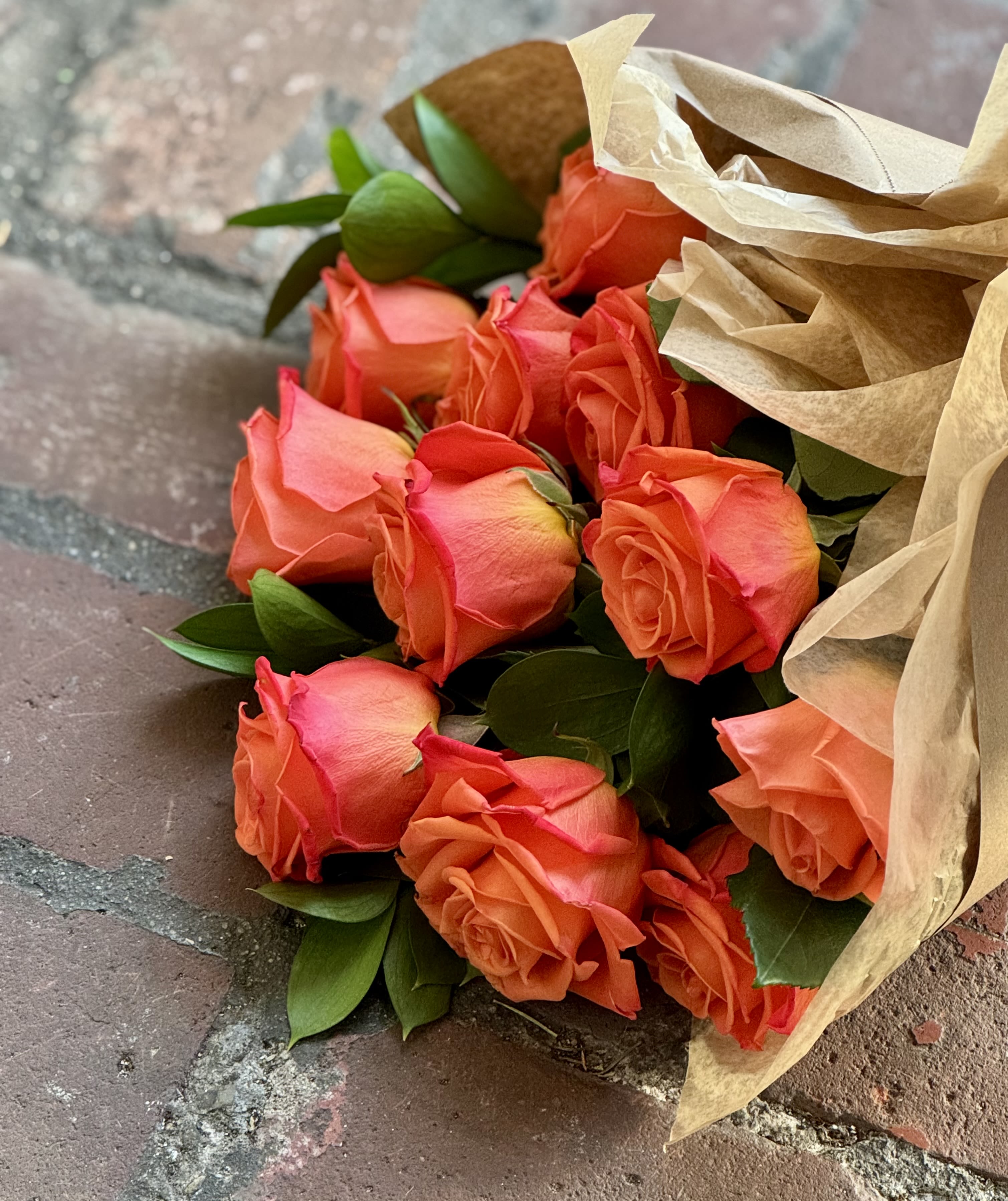 Orange Crush Paper Wrapped Bouquet  - Fresh orange roses paper wrapped with a bow!  Select DELUXE for two dozen roses Select PREMIUM for three dozen roses  NOTES: We will choose the freshest and most interesting ingredients at the market to make this arrangement shine. Vessels may be substituted depending on availability.