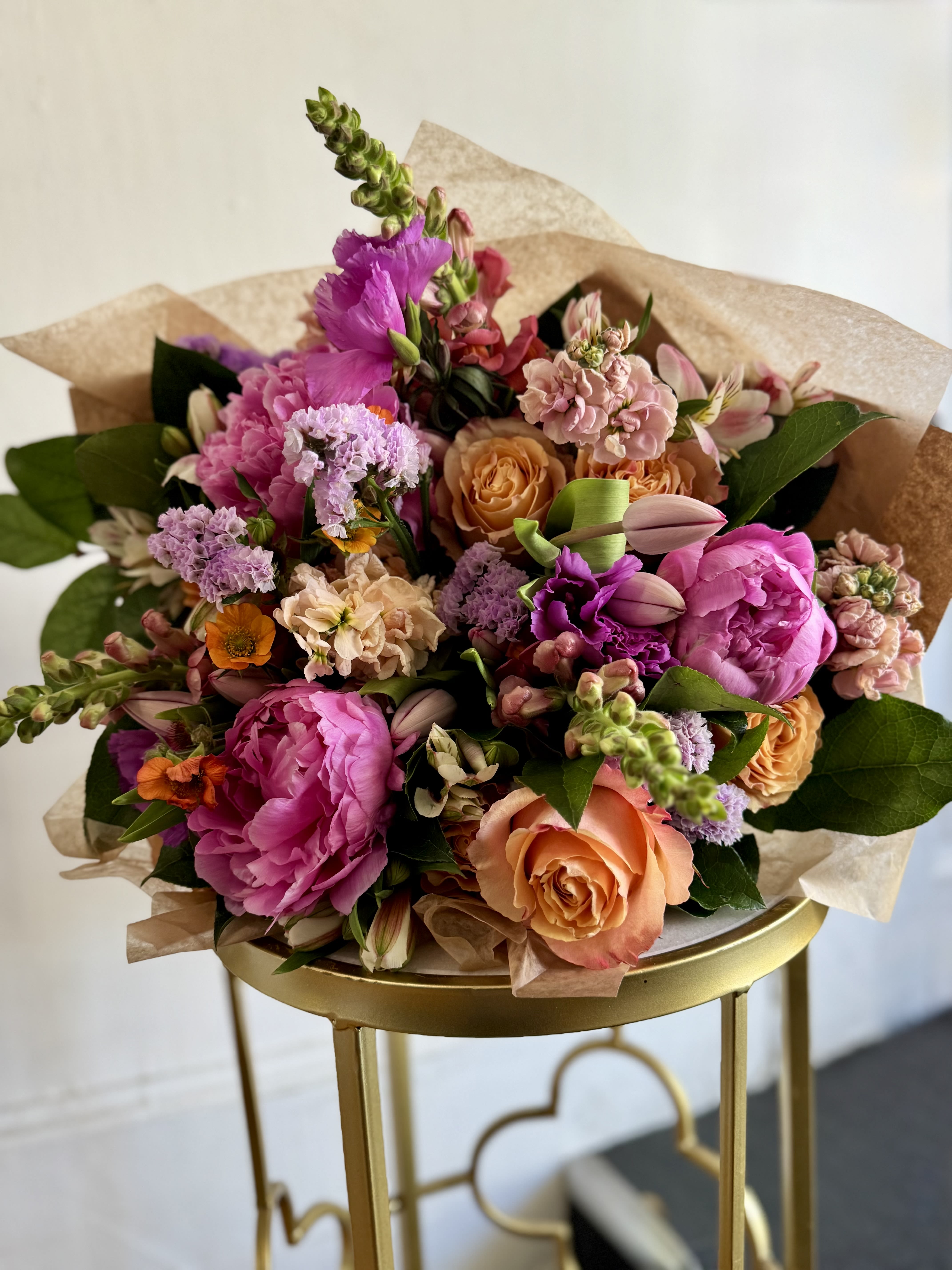 Pretty Premium Designers Choice  - Lush pink peonies and soft peach roses make this Mother's Day premium designers choice bouquet feel like a private garden picked just for her - a romantic, feminine arrangement perfect for an anniversary, or to celebrate a special birthday.   This bouquet mixes pink  and clusters of lavender-hued filler for a layered palette of pink, peach, purple, and white. Finished in a natural brown paper wrap, the presentation is polished with a rustic touch; the color contrast between saturated pinks and softer lilacs creates a lively springtime mood. Hand-tied styling gives the bouquet a generous, tactile shape that looks beautiful in a vase. 