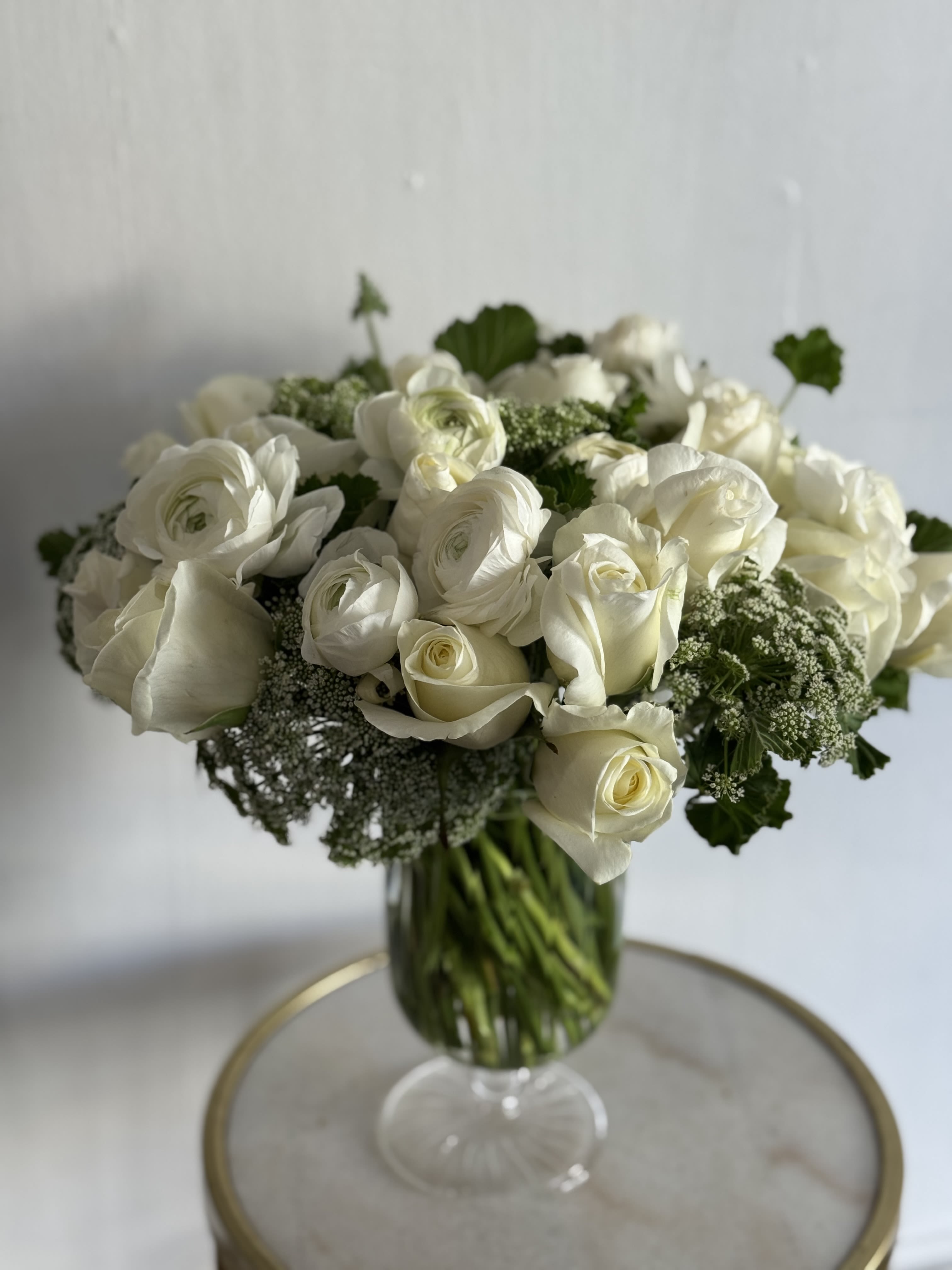 Cloud 9 - A soft, cloud-like cluster of white roses and ranunculus makes this flower arrangement an ideal choice for a Mother Day Gift , wedding , sympathy tribute, or a gentle thank-you gift. The predominantly white and green palette reads calm and elegant, so the recipient will sense care and serenity the moment the vase is set down.  A lush, full silhouette that works on a dining table, entry console, or beside.   Perfect for moments that call for understated beauty-new baby visits, sympathy, anniversaries, or a sincere thank-you. This arrangement arrives ready to display. For best longevity, place in fresh water away from direct heat and change the water every couple of days to keep the blooms looking their calm, cloud-like best.