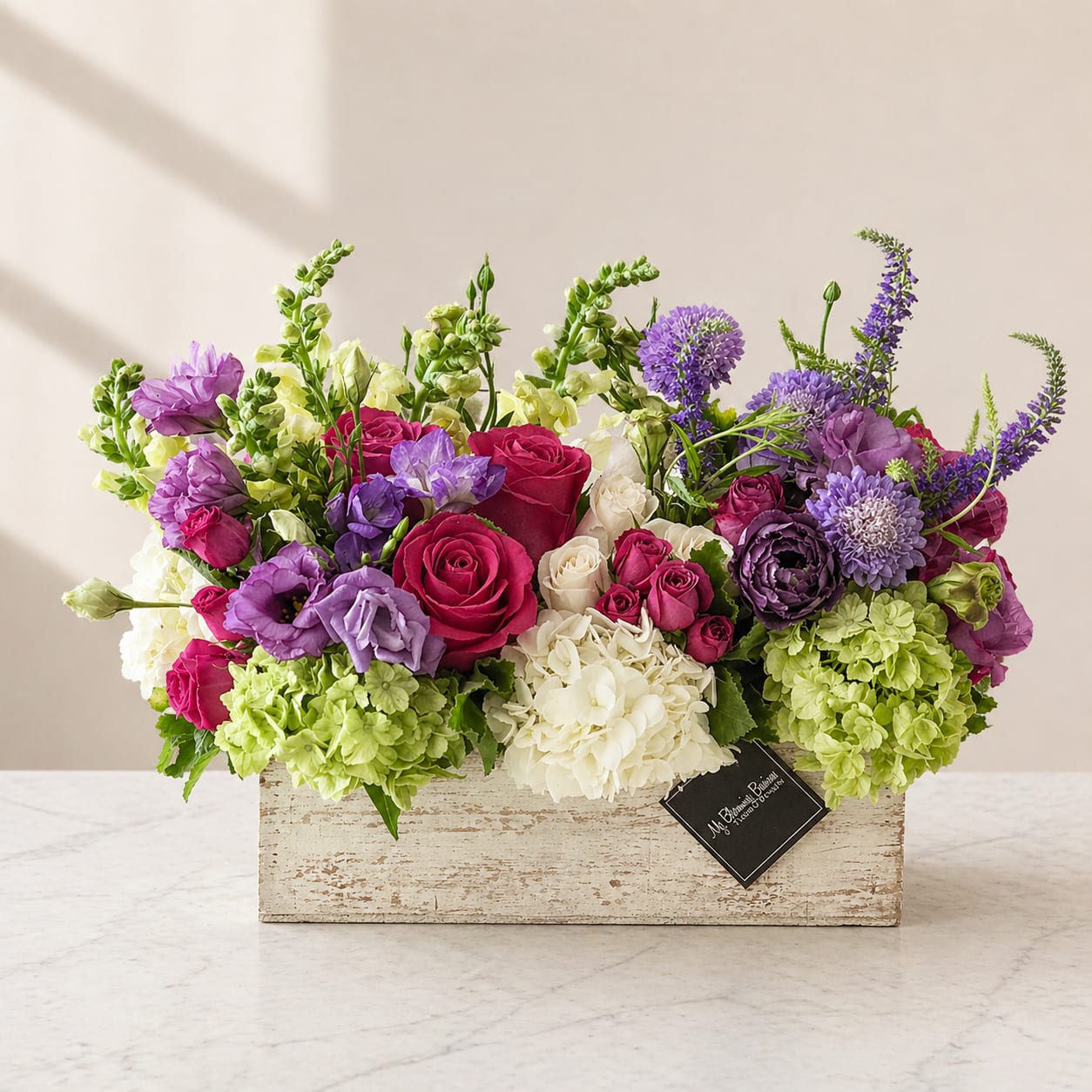 Rustic &amp; Chic  - Rustic charm meets effortless elegance in this beautifully designed floral arrangement. Handcrafted in a distressed wooden box, this garden-inspired design features a lush mix of premium roses, hydrangeas, lisianthus, seasonal blooms, and textured greenery. Rich jewel tones blend seamlessly with soft creams and fresh greens, creating a look that feels both refined and welcoming.  Designed with a low, elongated silhouette, this arrangement is perfect for dining tables, kitchen islands, coffee tables, or entryway consoles. Its rustic container paired with elevated floral styling makes it a versatile statement piece that complements modern farmhouse, French cottage, and classic home décor.  Whether sent as a heartfelt gesture, a thank-you, an anniversary surprise, or simply to brighten someone’s space, Rustic &amp; Chic delivers timeless beauty and warmth with every stem.  Details:  Hand-arranged with fresh, premium seasonal flowers  Designed in a rustic wooden box for a natural, elevated look  Garden-style composition with rich color and texture  Ideal for home décor, celebrations, and meaningful moments  Flower varieties and tones may vary slightly based on seasonal availability, ensuring a fresh and unique arrangement every time.