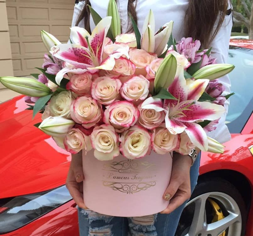 Round pink hatbox of cream roses and pink lilies held in front of a red car