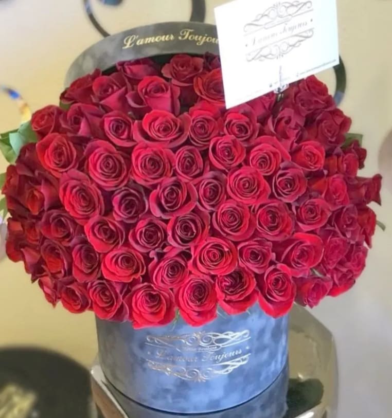 Round box filled with tightly packed red roses and a small card on top