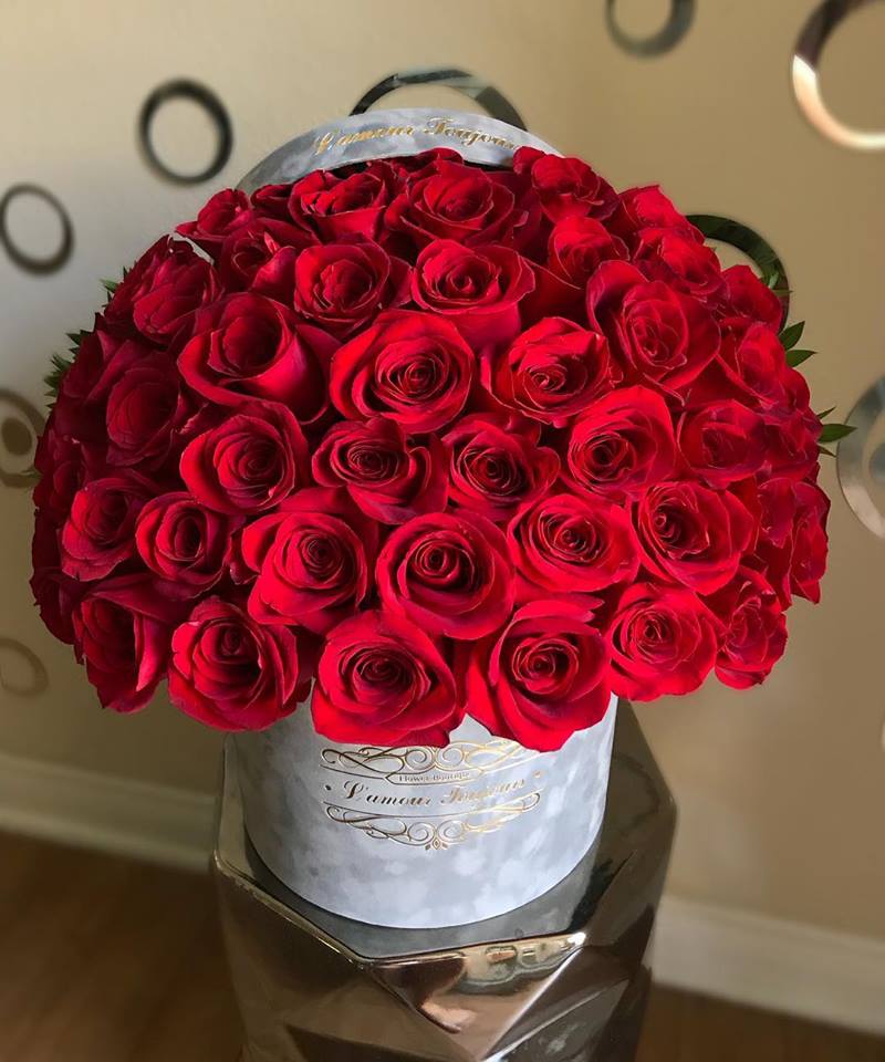 Round hatbox filled with tightly packed red roses on a reflective pedestal