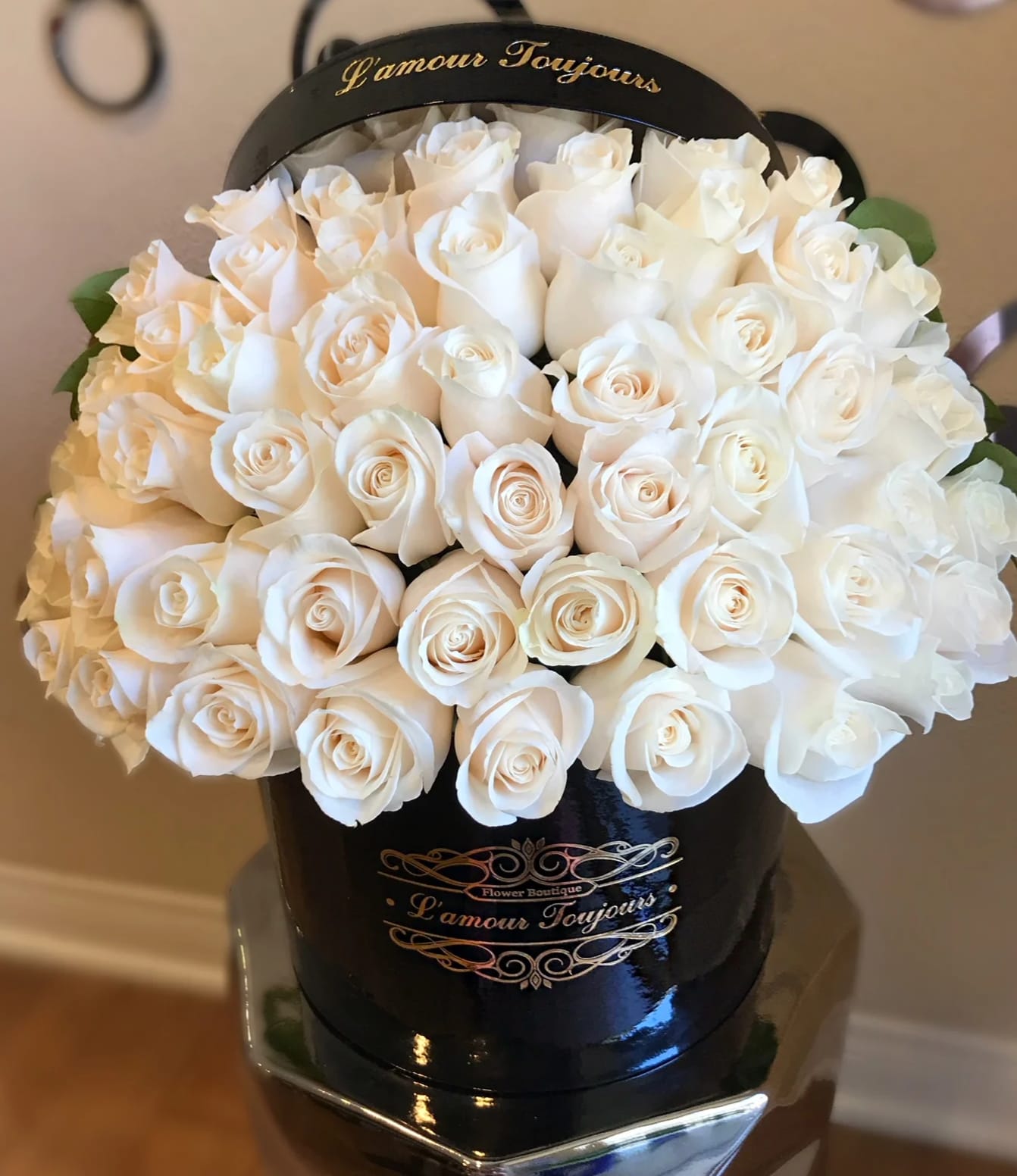 Round black hatbox filled with tightly packed cream white roses