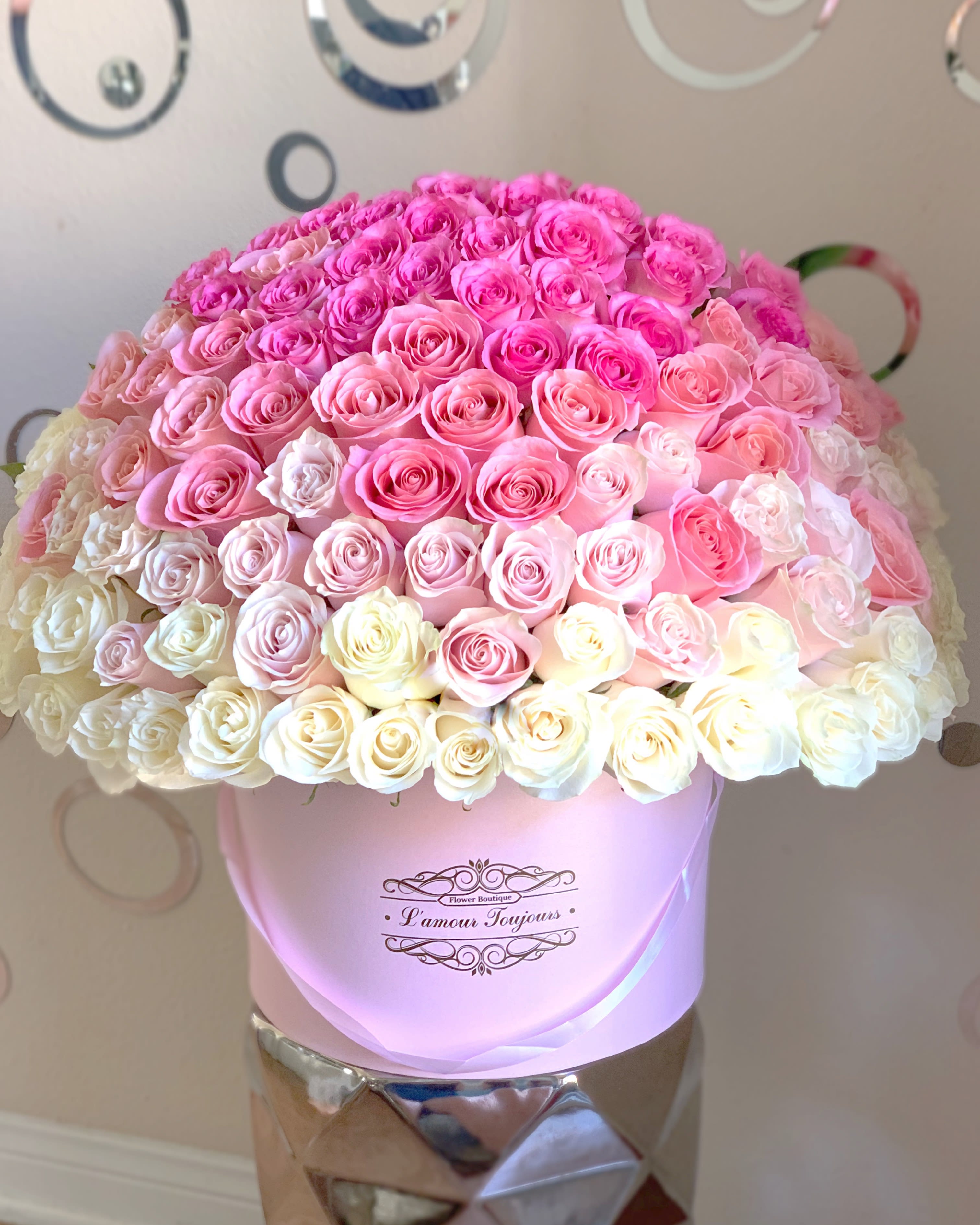 Large dome of pink and cream roses arranged in a round pastel pink hatbox.
