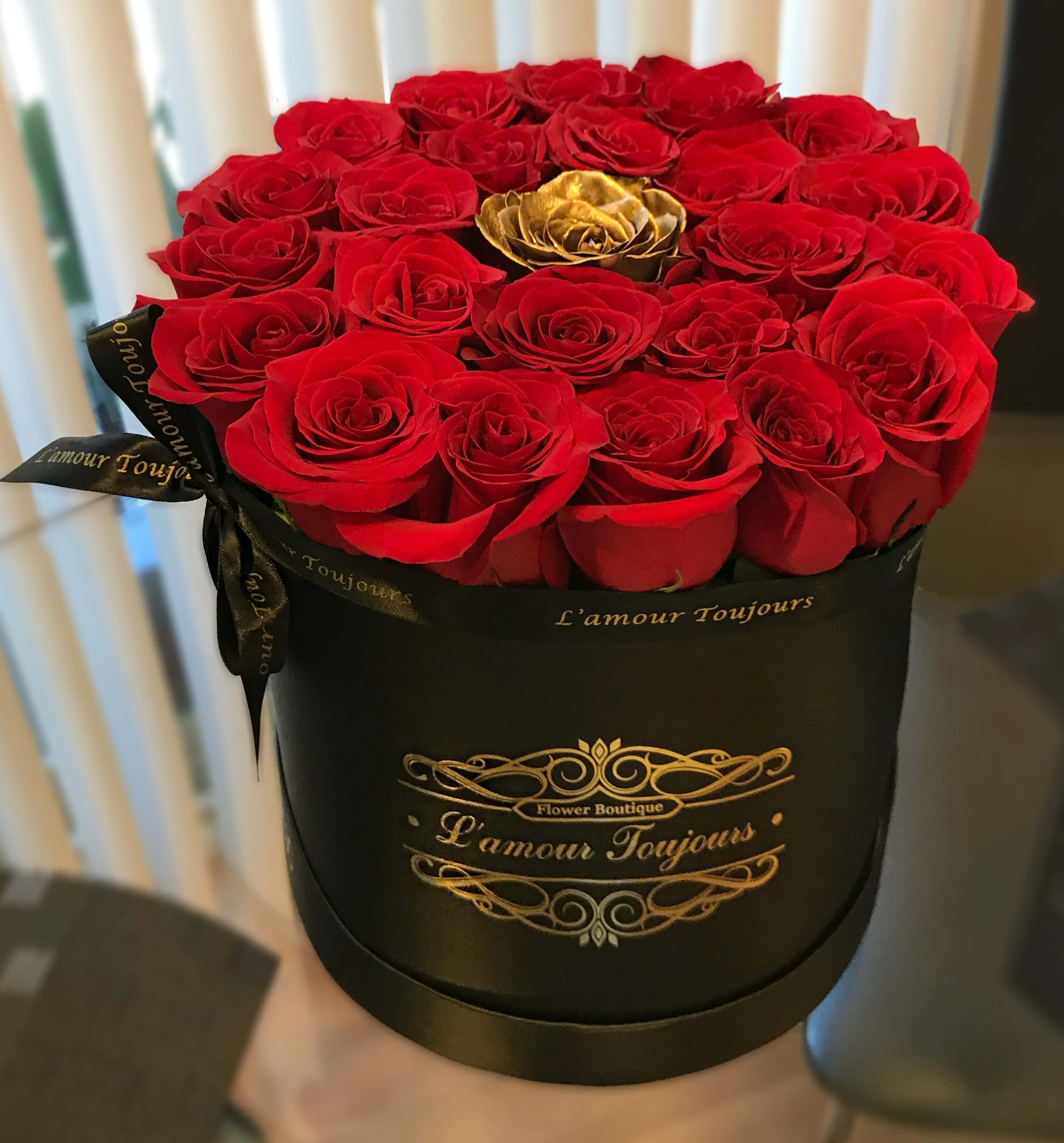 Red roses arranged in a black round box with a gold rose accent