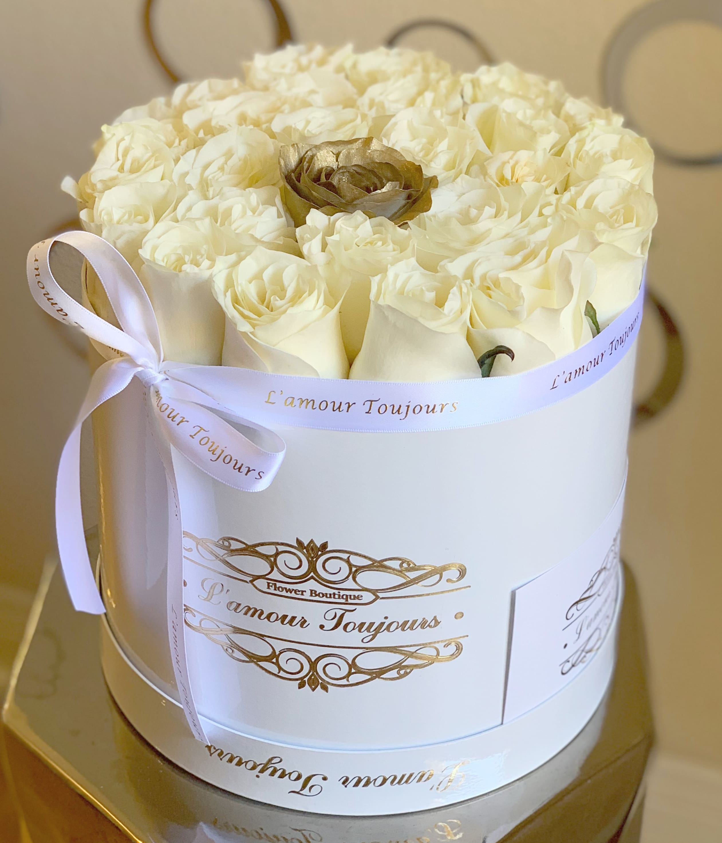 Round white box filled with cream roses and a single gold rose, tied with a white ribbon.