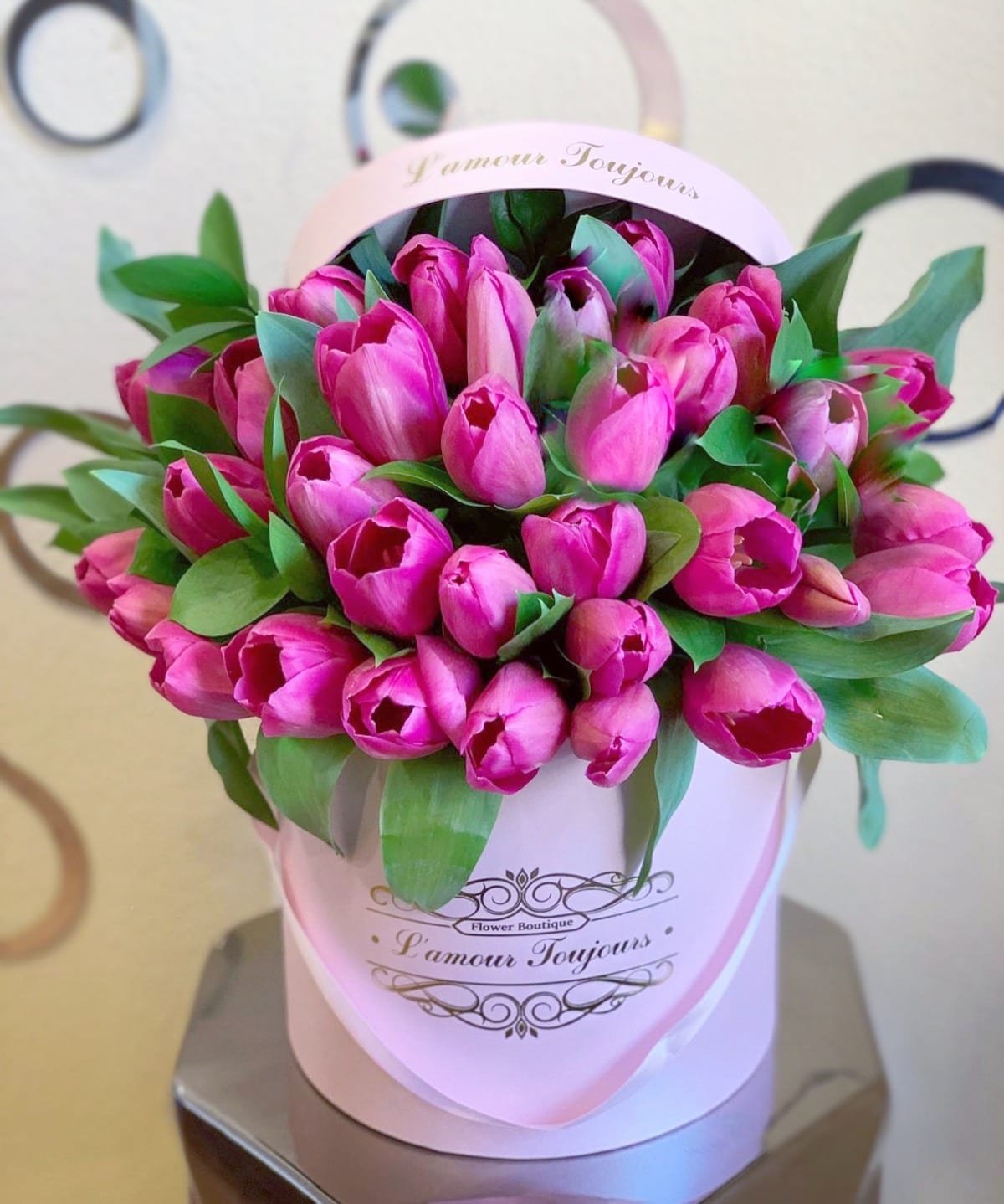 Pink tulips arranged in a round pink hatbox with green leaves