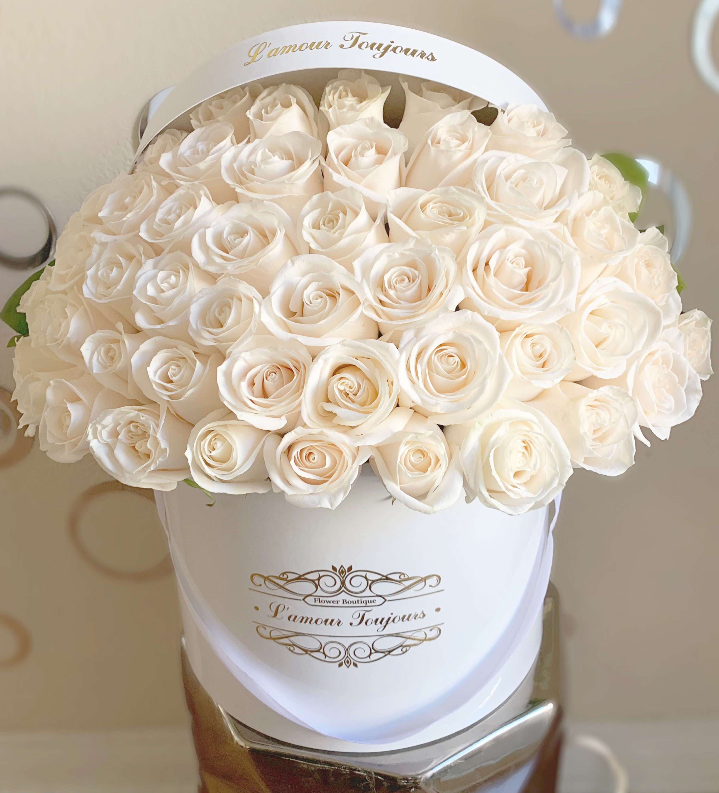 Round white hatbox filled with tightly packed ivory roses with gold script on the front